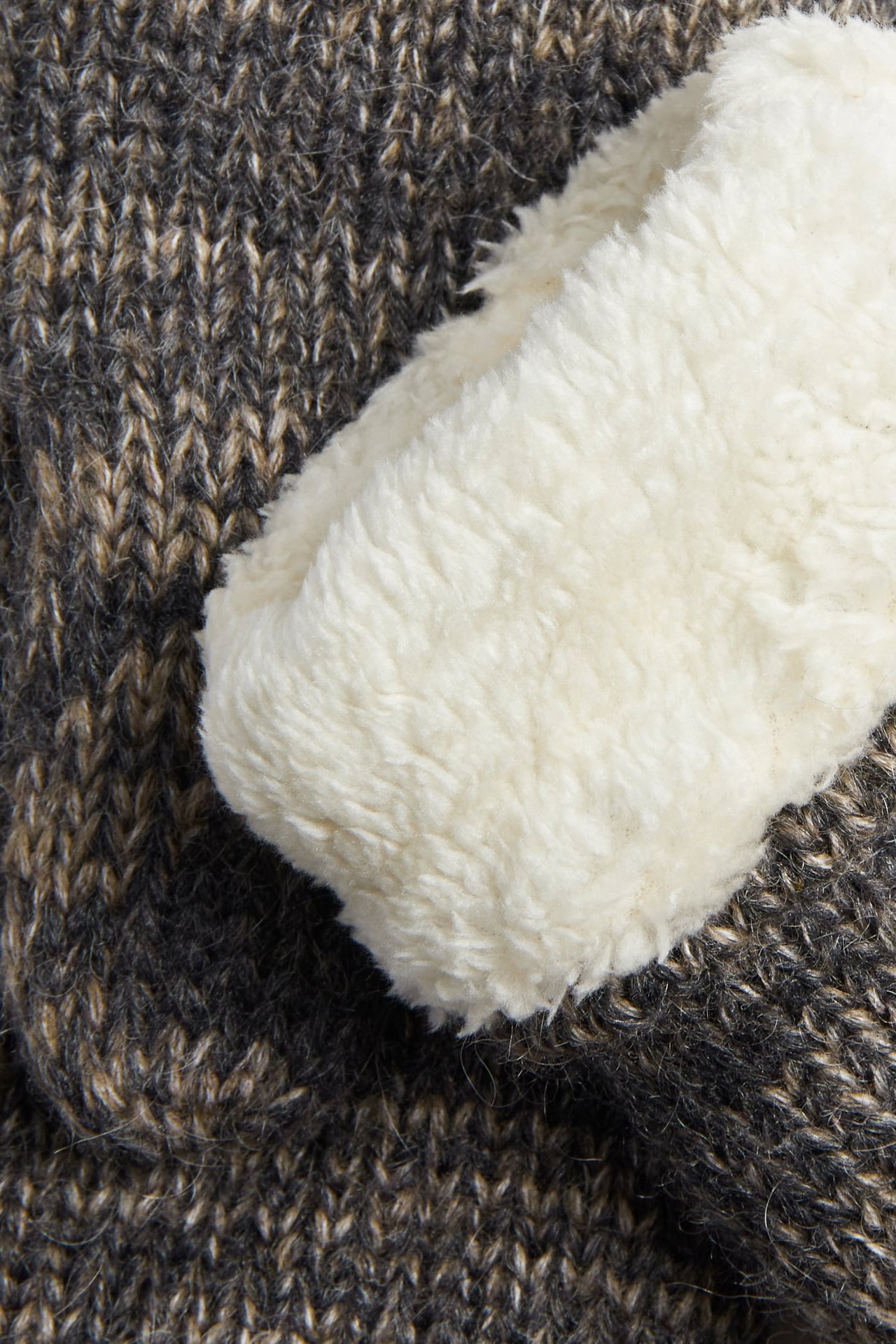 Lähikuva kermanvärisestä tekoturkisfuorista tummanruskeassa kirjavassa neuleessa.