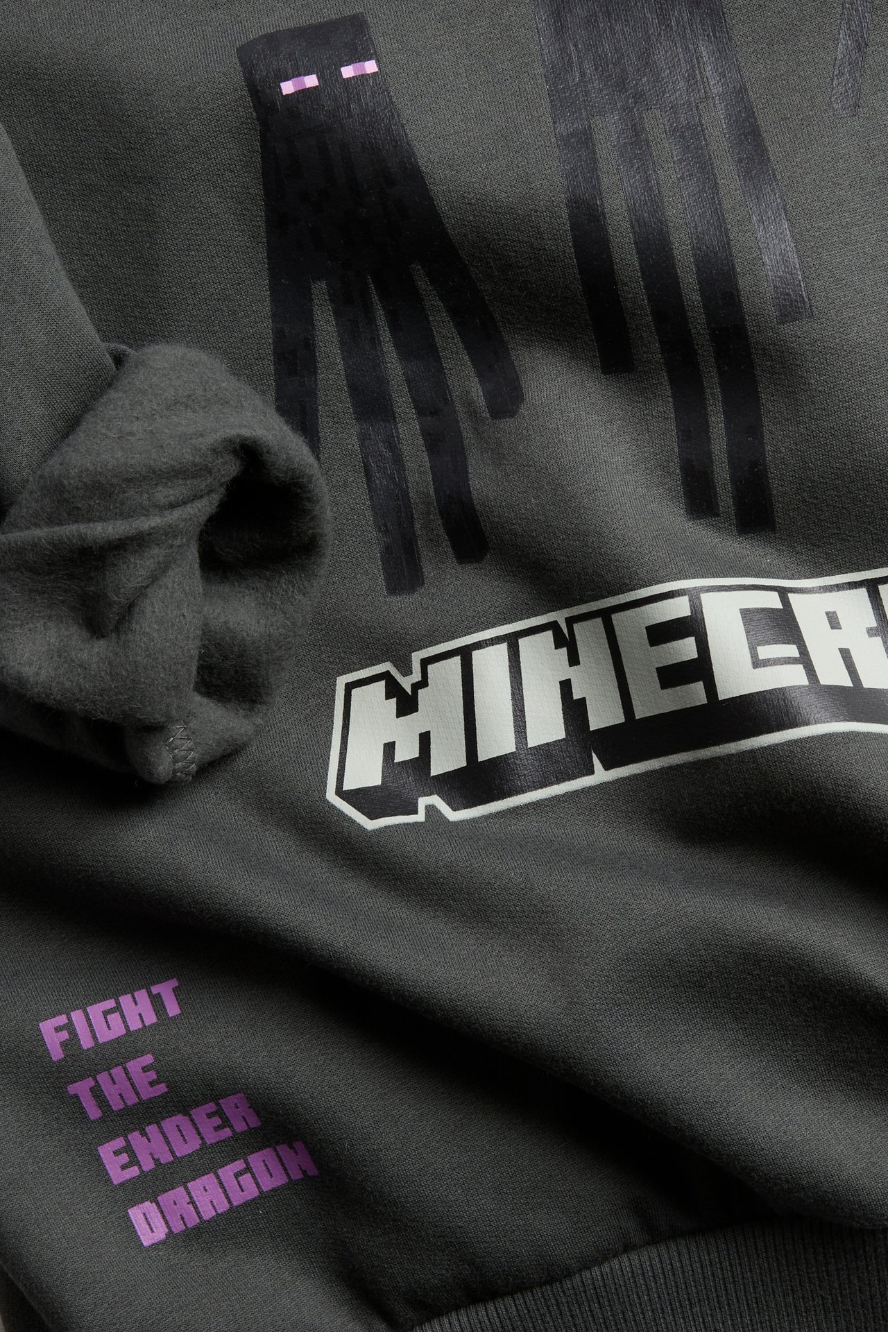 Närbild av en mörkgrå sweatshirt med Minecraft Enderman, logotyp och texttryck på framsidan.