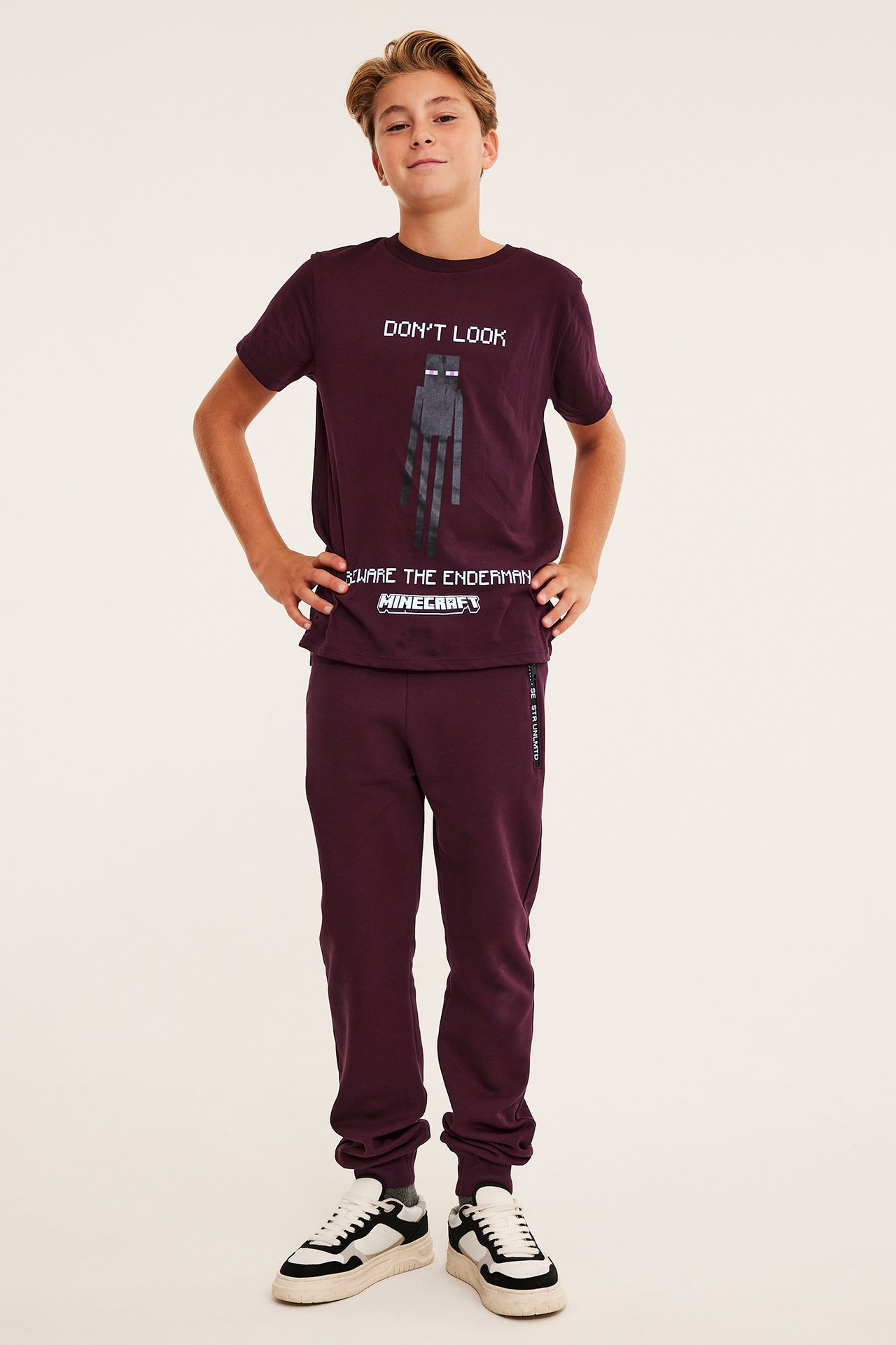 Framifrån på barn i maronfärgat Minecraft t-shirt och mjukisset med vita och svarta sneakers.
