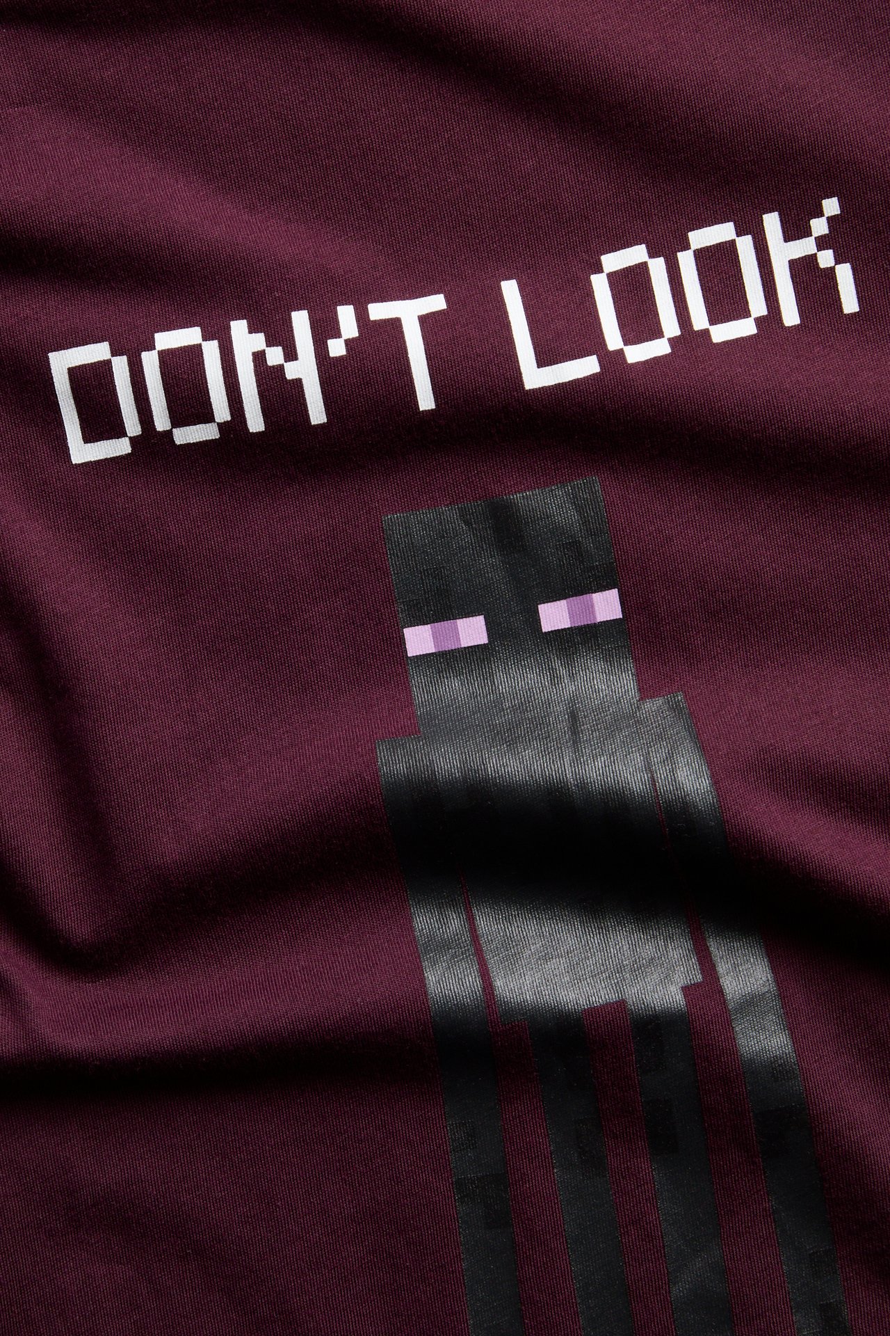 Närbild: Vinröd t-shirt med vit 'DON'T LOOK' och svart pixlat Enderman-tryck.
