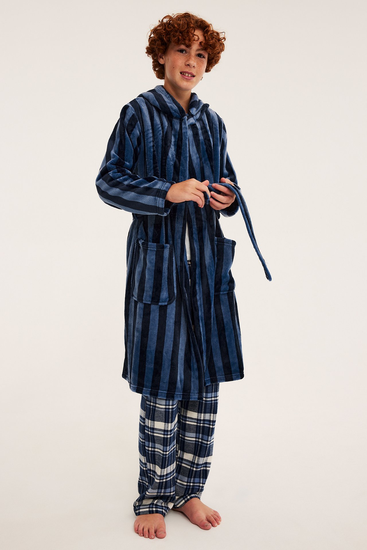 Framsida av en pojke som bär en blårandig morgonrock med huva över blårutiga pyjamasbyxor.