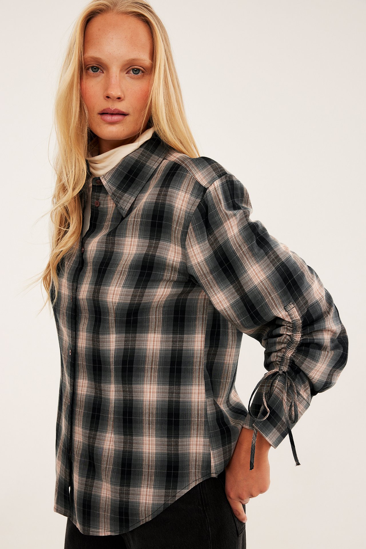 Frontbilde av en kvinne i mørk rutete skjorte med rynkede ermer over hvit turtleneck.