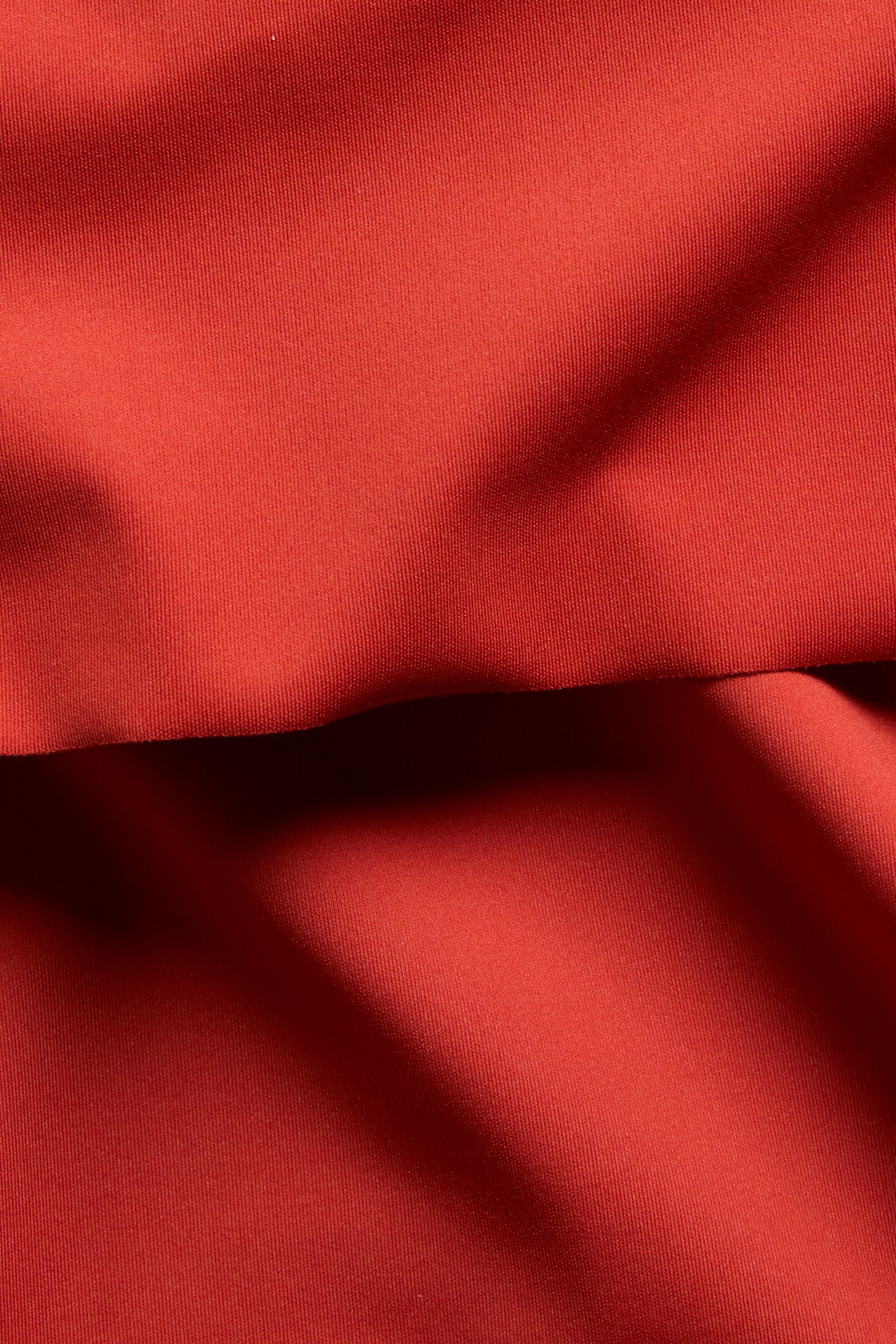 Lähikuva punaisesta yksivärisestä bikinihousun kankaasta, jossa taitettava vyötärödetalji.