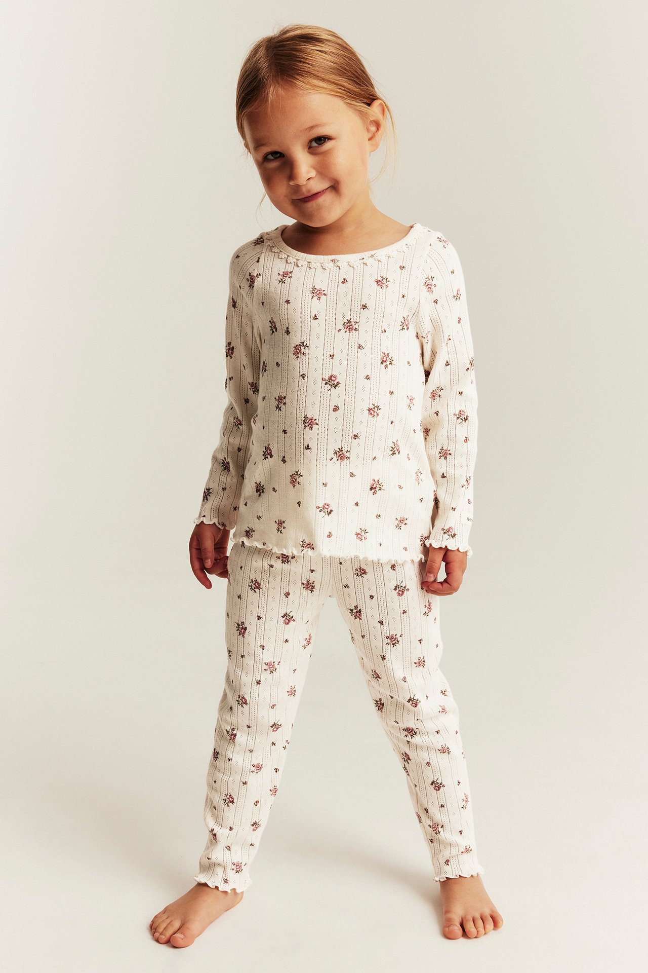 Frontbild på barn i vit ribbad långärmad tröja och matchande byxor med blommigt mönster.