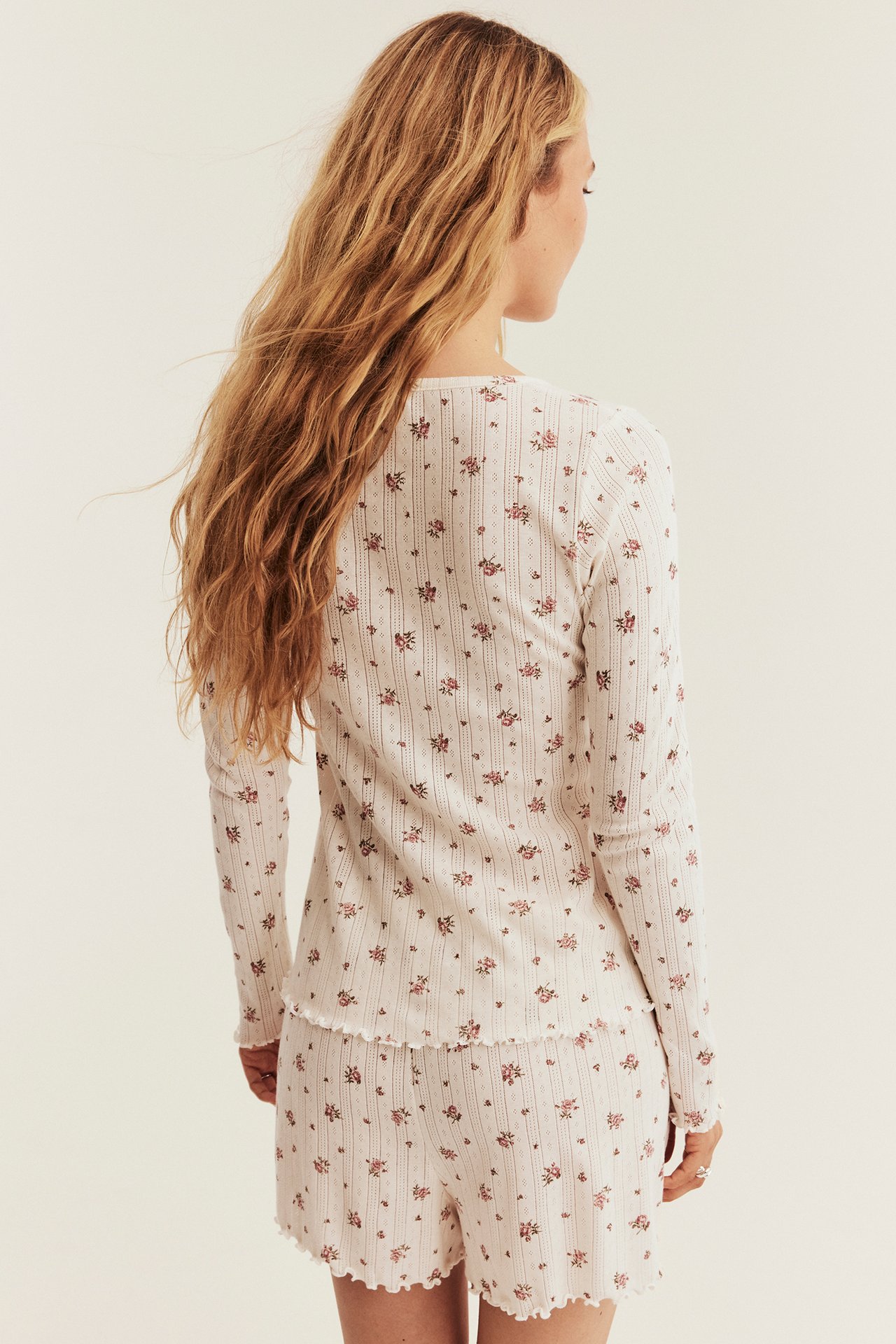 Kvinna bakifrån i vitt ribbat blommigt pyjamasset med volangkanter.