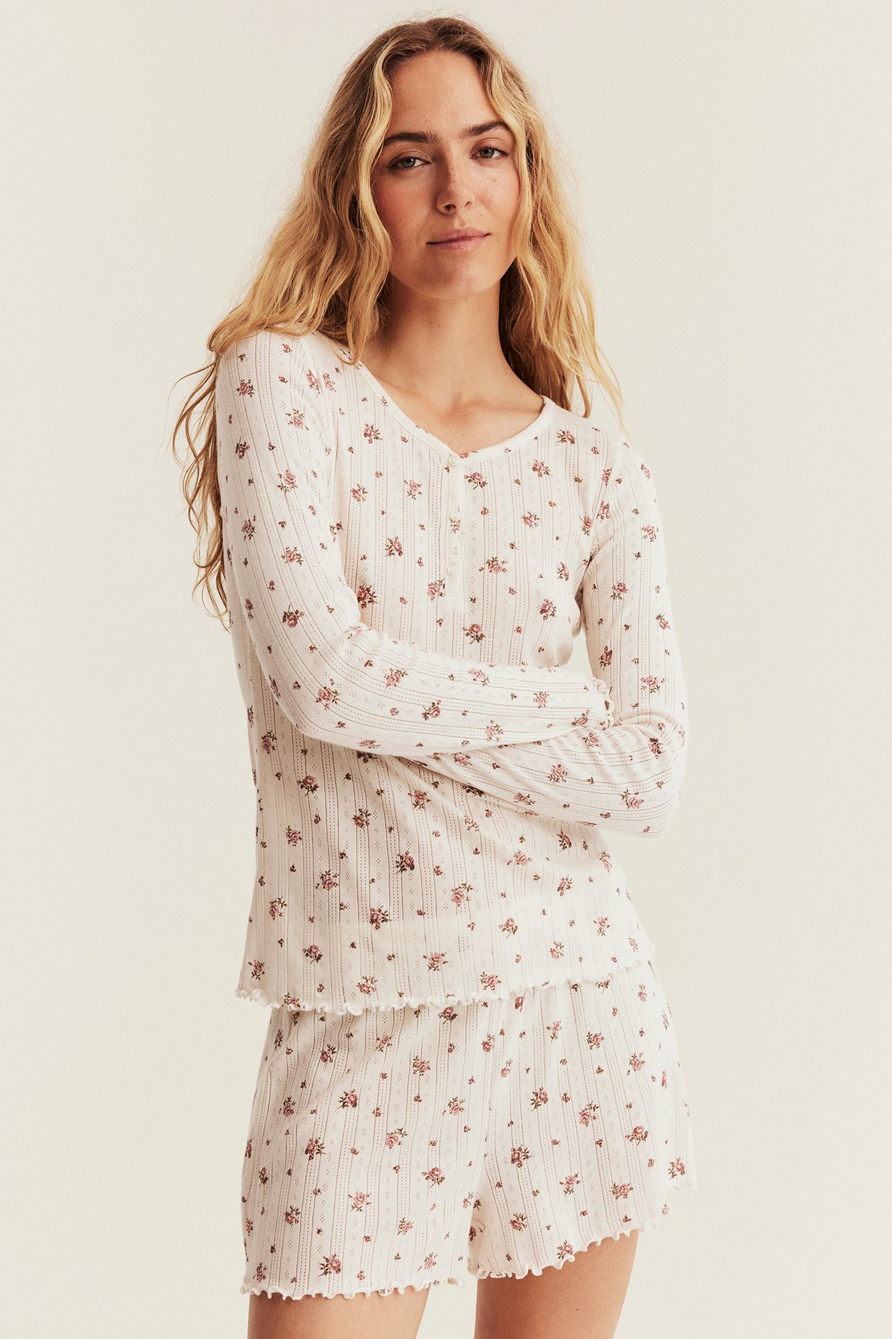 Framifrån, kvinna i ett vitt ribbat blommigt pyjamasset med långärmad topp och shorts.