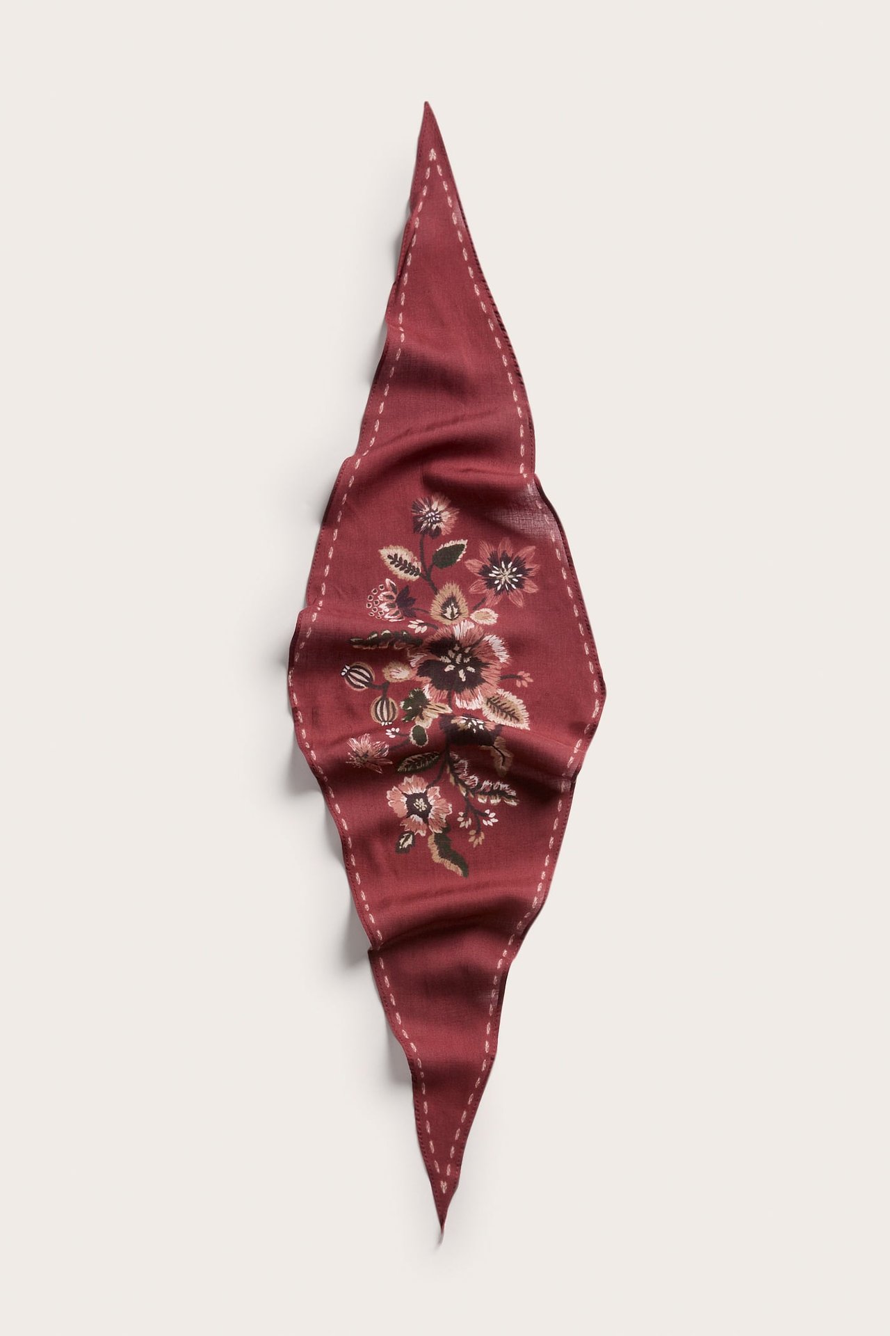 Ovenfra mørkerødt rombeformet skjerf med blomstermønster og hvite stiplete kanter.
