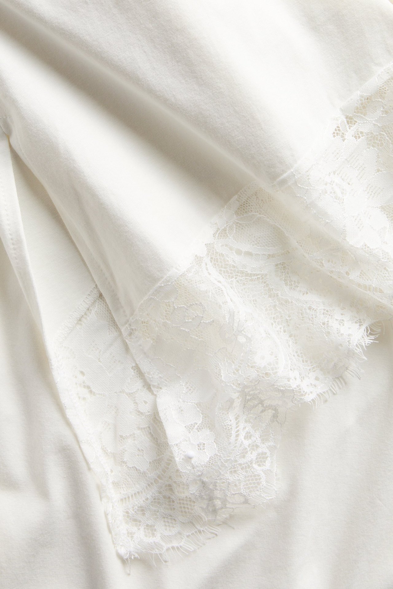 Zbliżenie białego asymetrycznego topu z białymi koronkowymi detalami na dole.