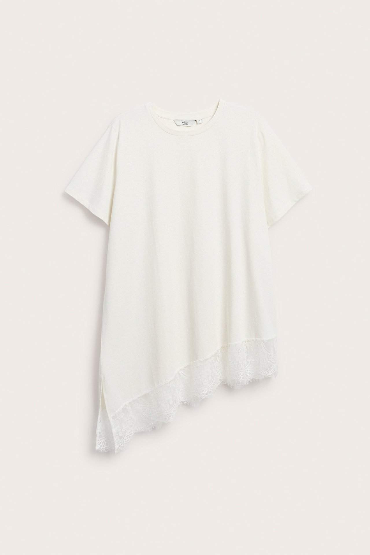 Widok z przodu białego, krótkiego topu z asymetrycznym dołem i koronkową lamówką.