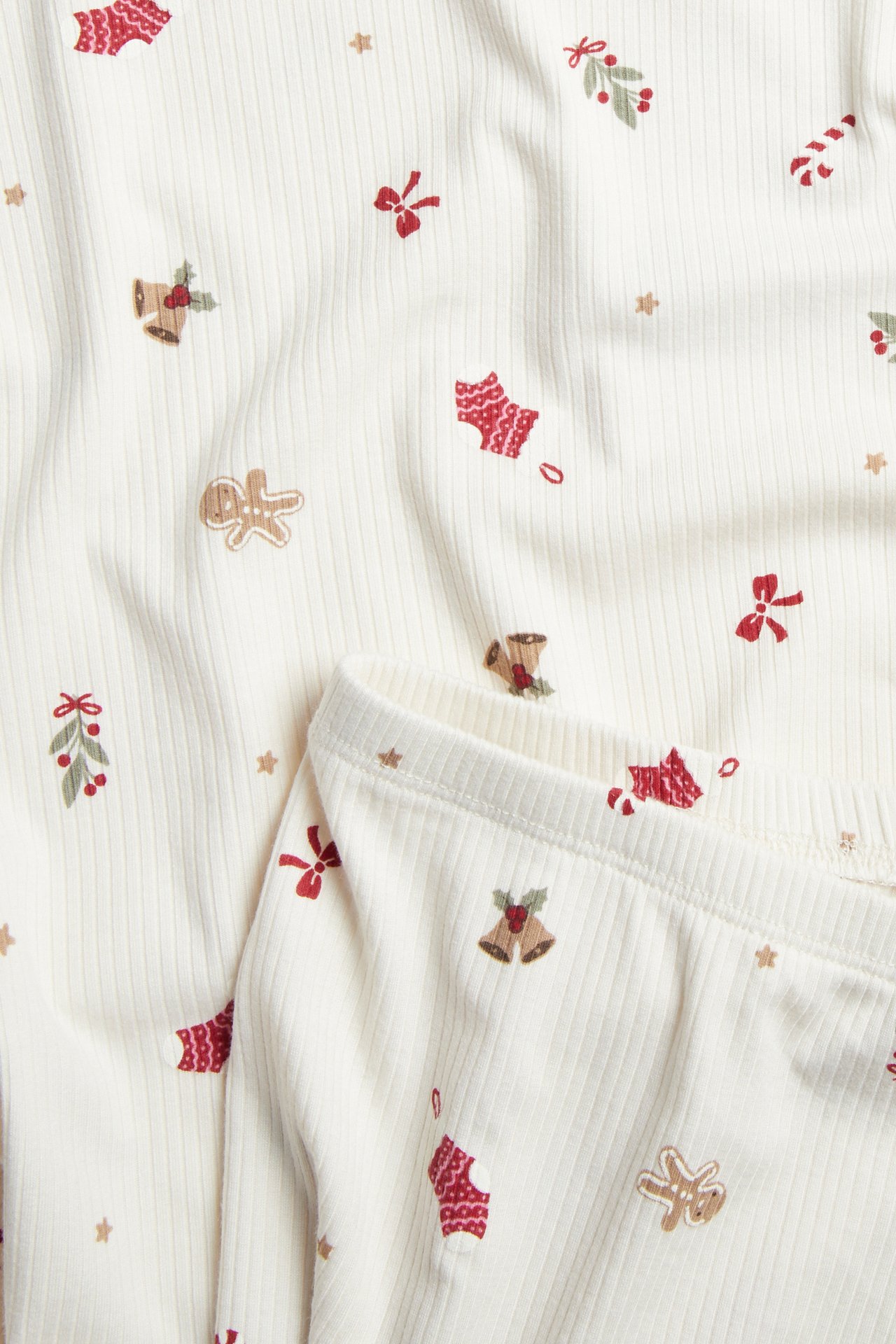 Nærbilde av ribbet offwhite babypyjamas med rødt og brunt juletrykk.