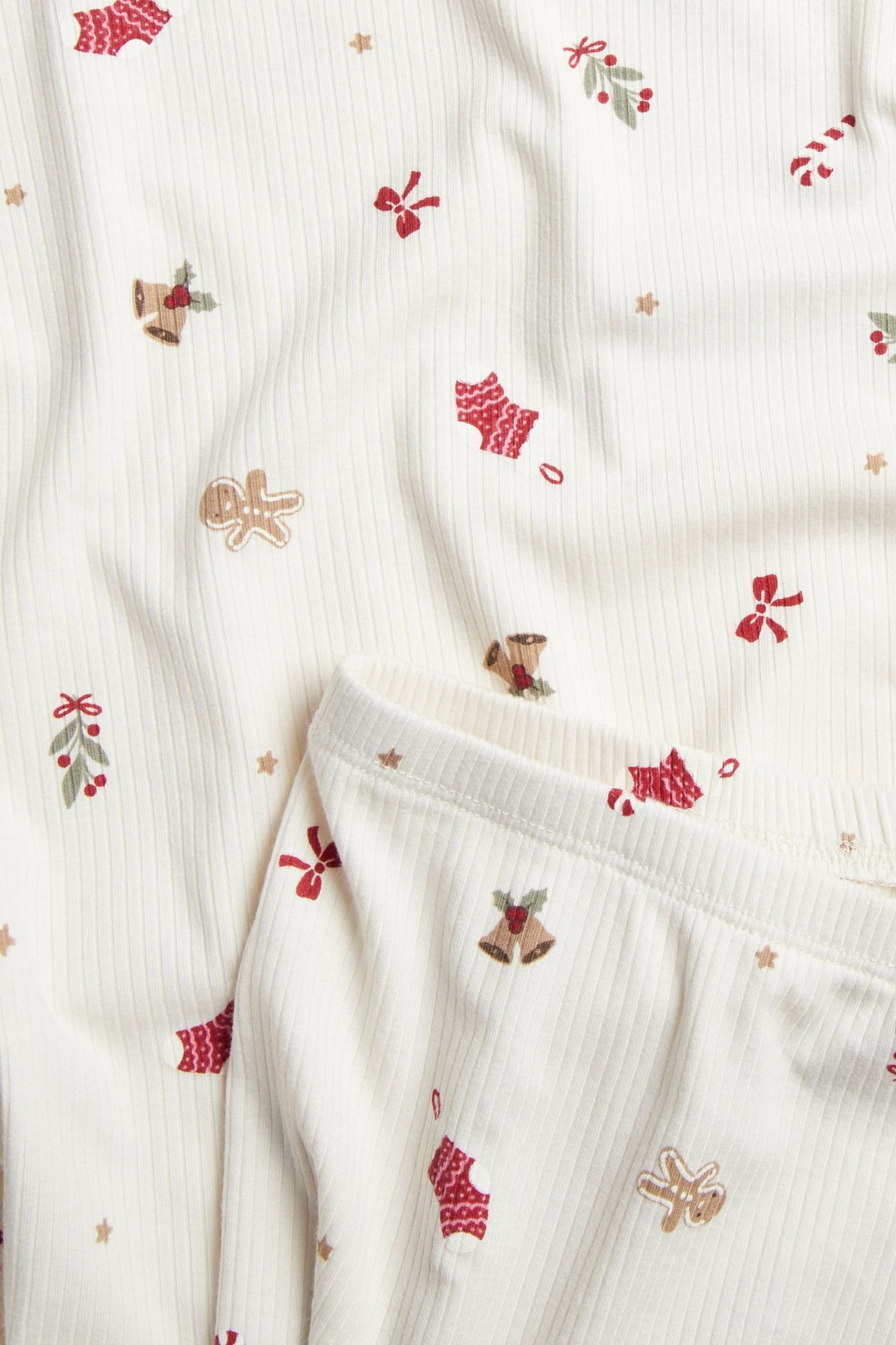 Nærbilde av ribbet offwhite babypyjamas med rødt og brunt juletrykk.