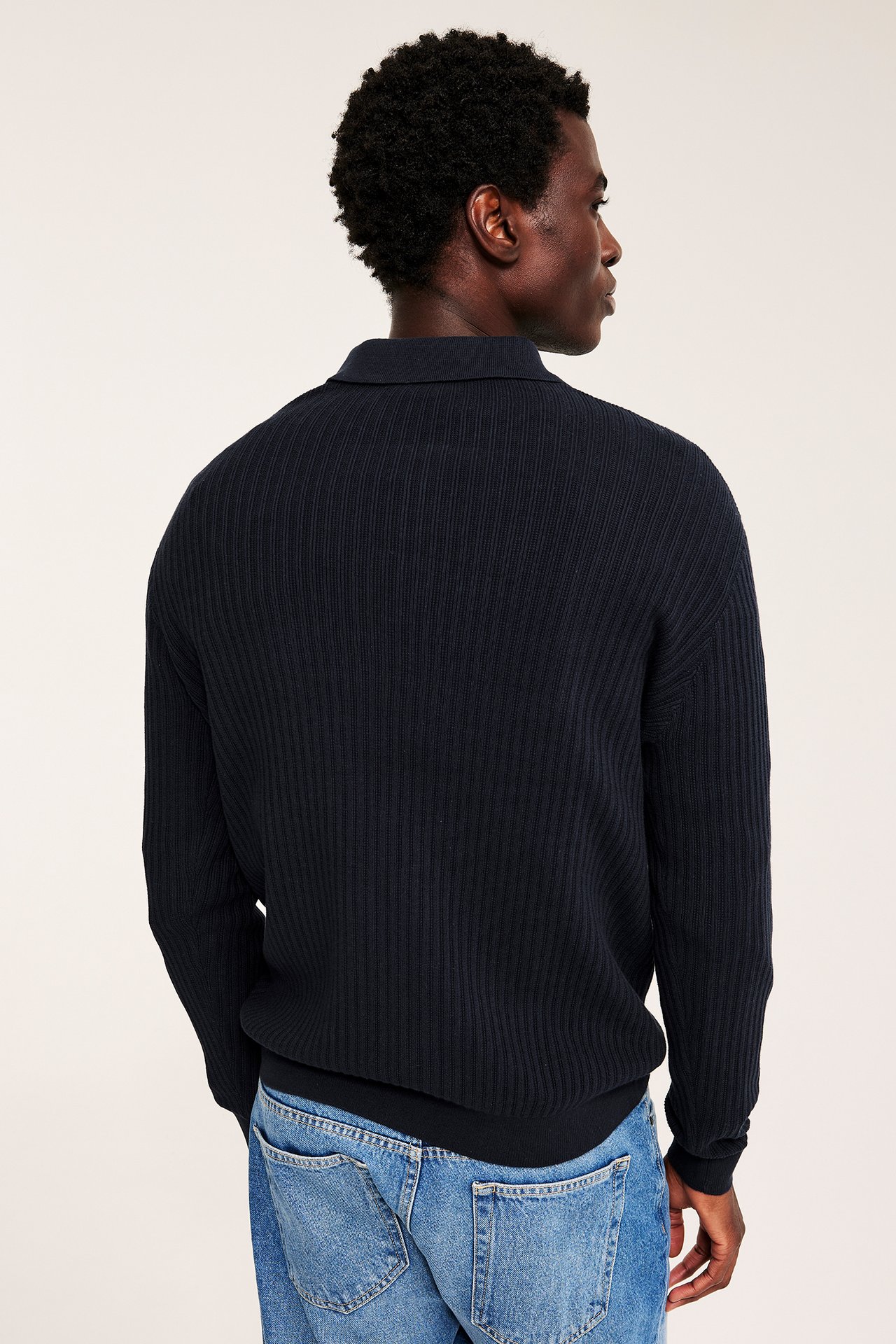 Mann sett bakfra, marineblå ribbestrikket langermet piké genser over lyseblå jeans.