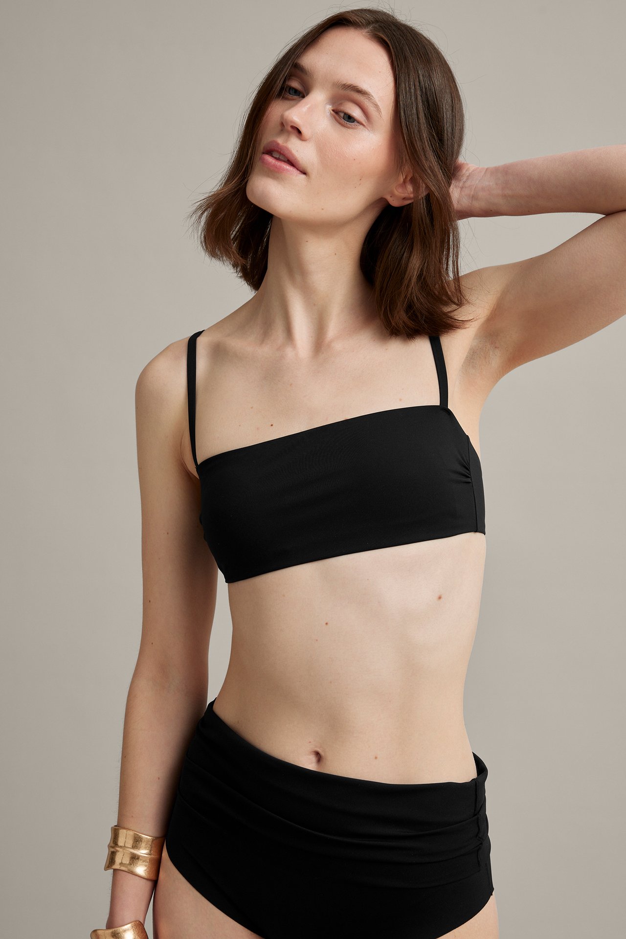 Frontbilde: Kvinne i svart polstret bandeau-bikinitopp, matchende rynket underdel, to gullarmbånd.