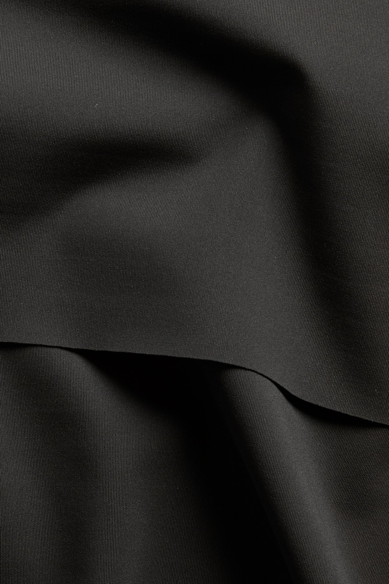 Lähikuva mustasta, yksivärisestä bikinialaosan kankaasta pehmeine laskoksineen.