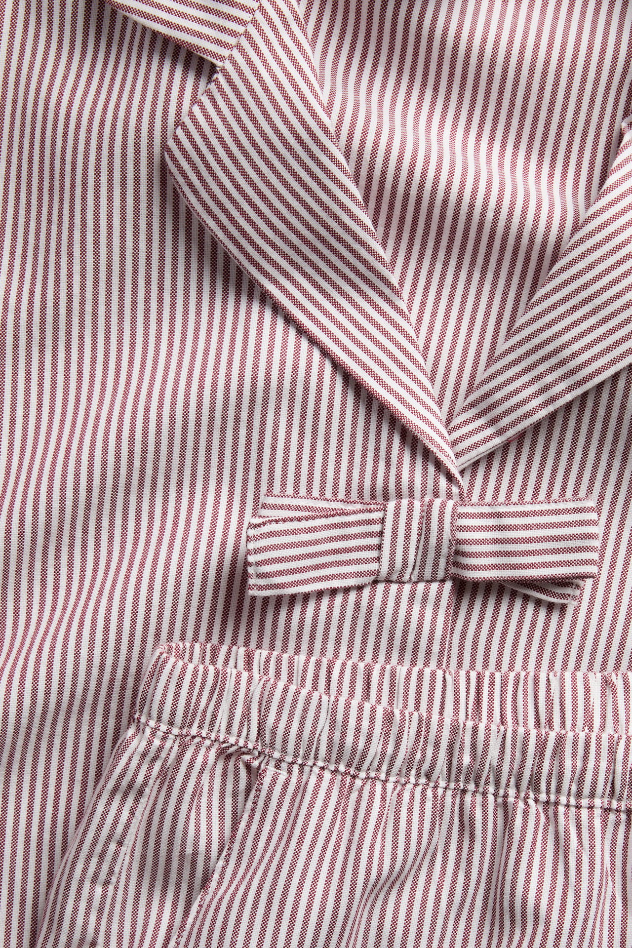 Lähikuva punavalkoraidallisesta pyjamasetistä, jossa käännekaulus, rusetti ja joustovyötärö.