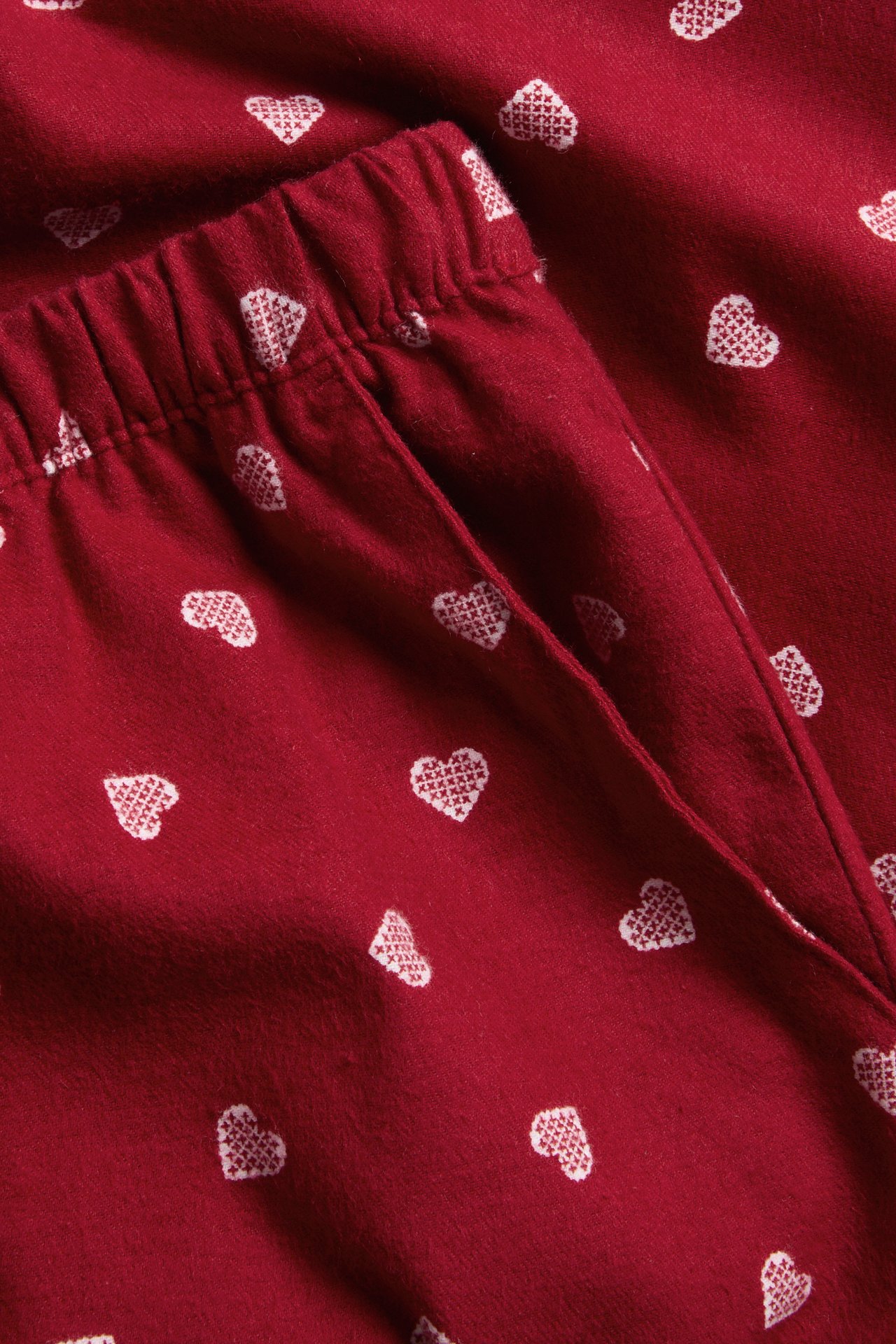 Närbild av röda pyjamasbyxor med vitt korsstygnsmönster av hjärtan.