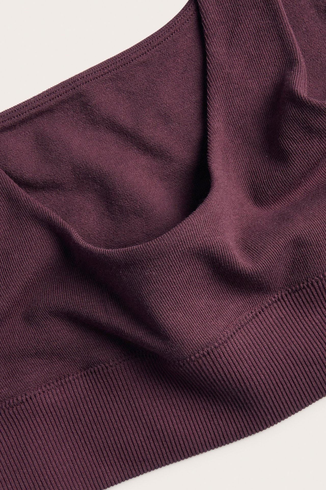 Närbild på en plommonfärgad ribbstickad bralette som visar tygets textur och en bred nederkant.