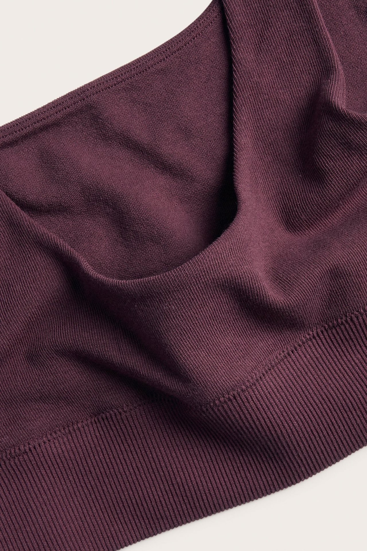 Närbild på en plommonfärgad ribbstickad bralette som visar tygets textur och en bred nederkant.