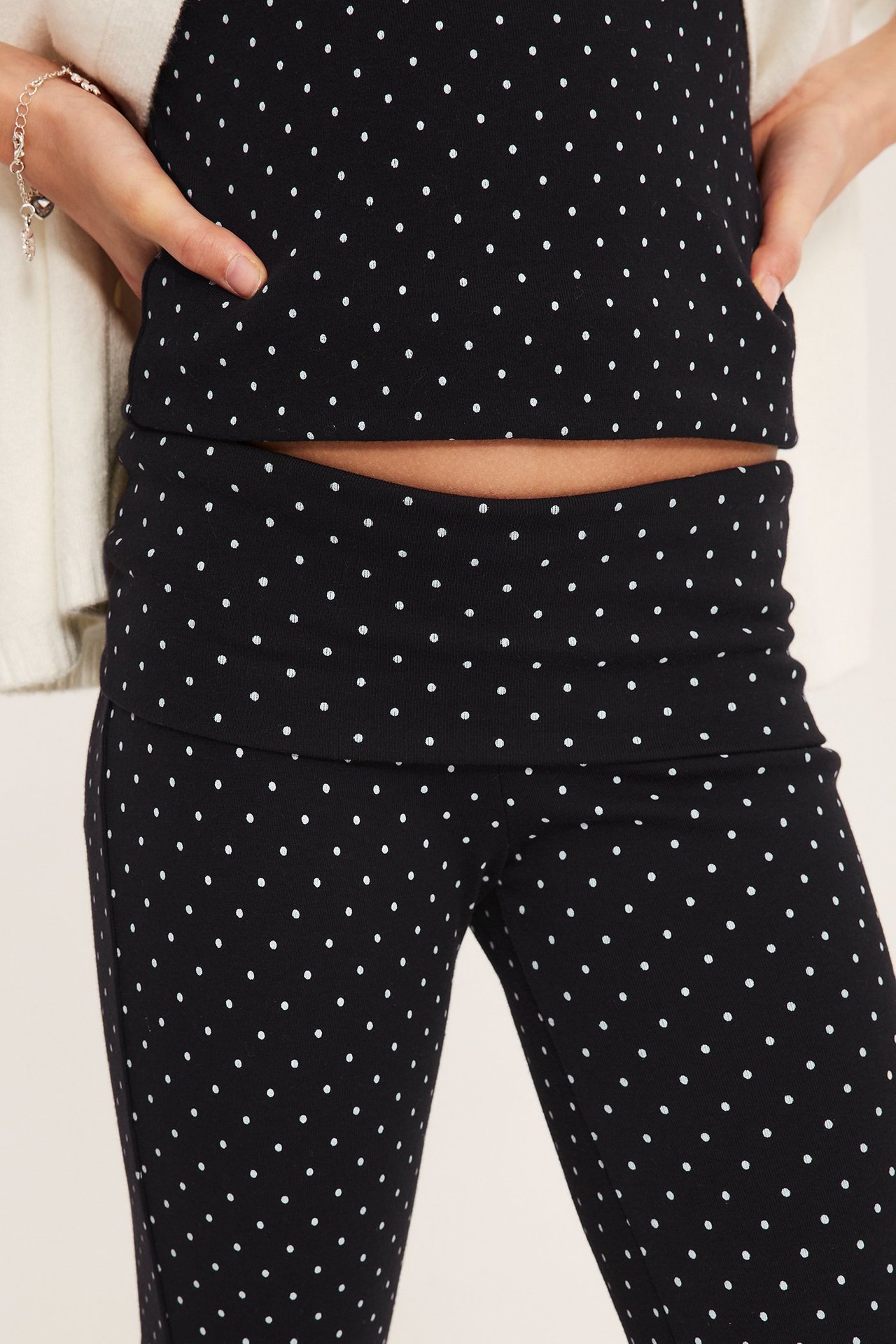 Zbliżenie dziecka: czarne legginsy w kropki z pasem, pasujący top, kremowy kardigan, srebrna bransoletka.