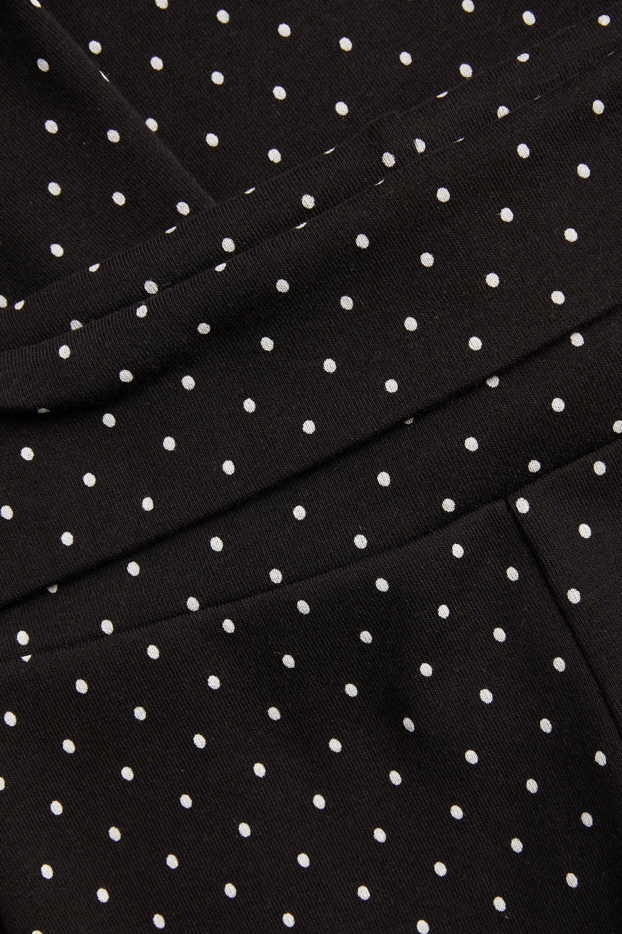 Zbliżenie czarnych kropkowanych spodni do jogi z bawełnianej dzianiny z wywijanym pasem.