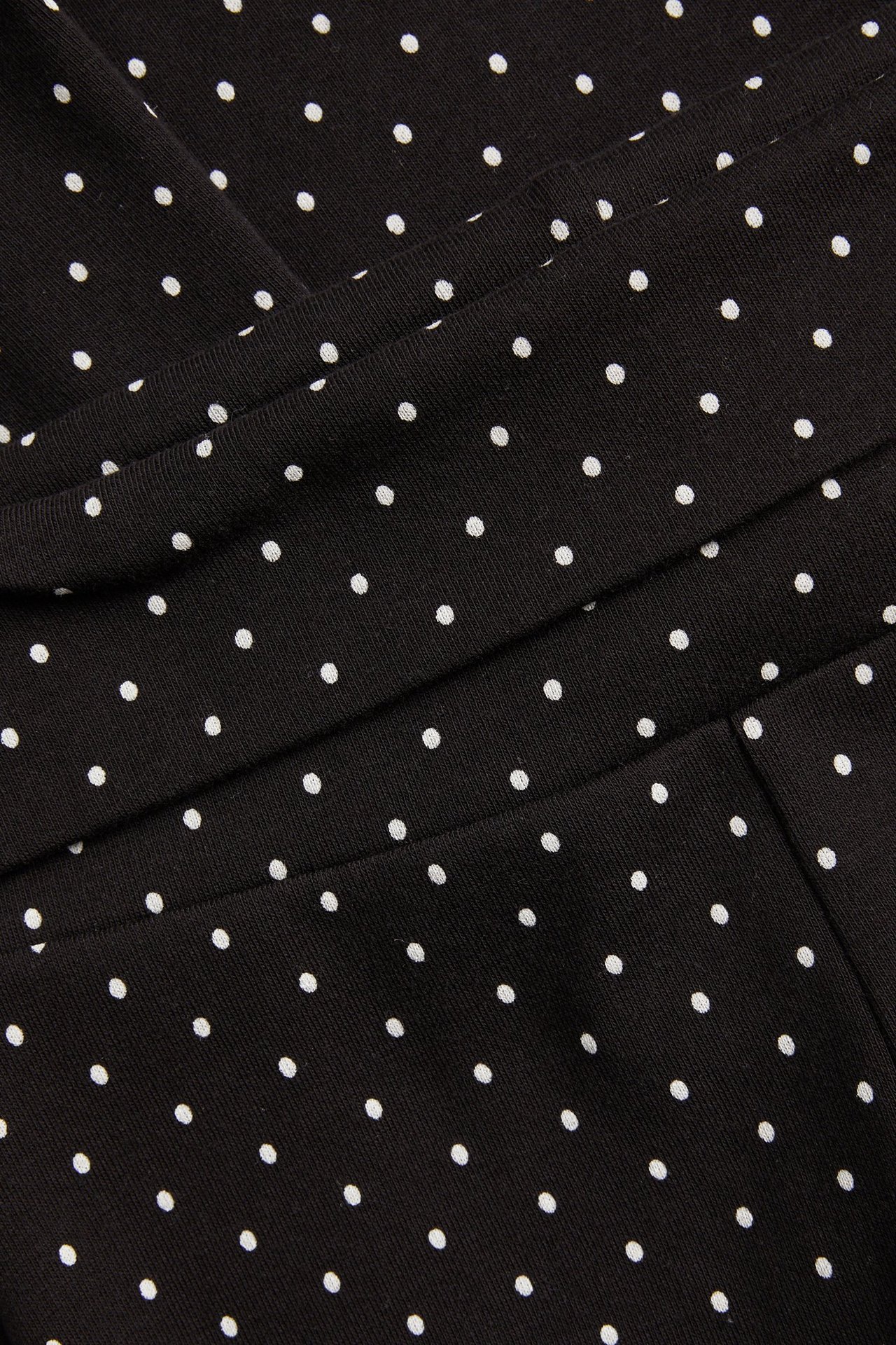 Lähikuva mustista pilkullisista puuvillatrikoota joogahousuista taitettavalla vyötäröllä.