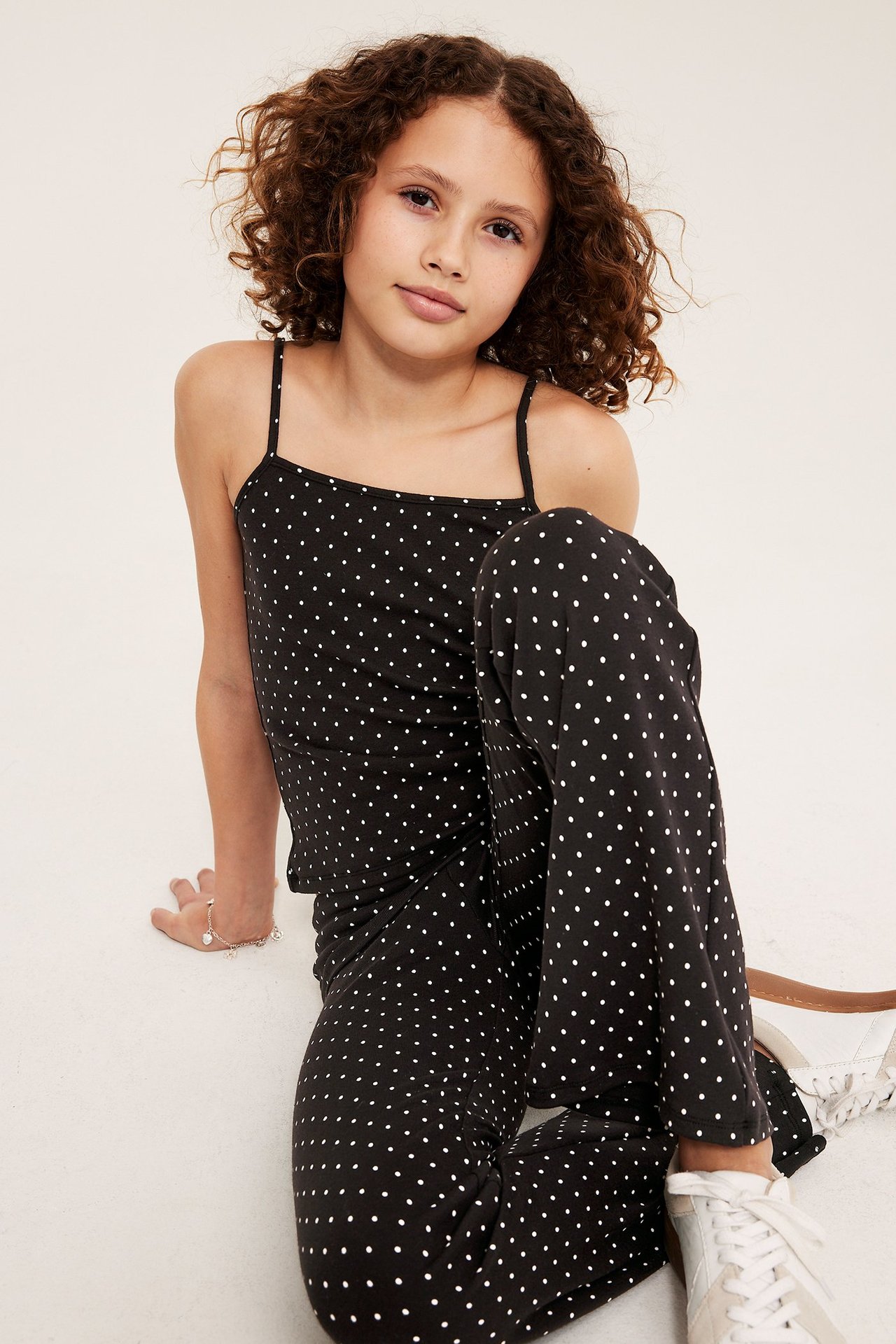 Framifrån, ett barn bär ett svart prickigt linne med smala axelband och matchande byxor.