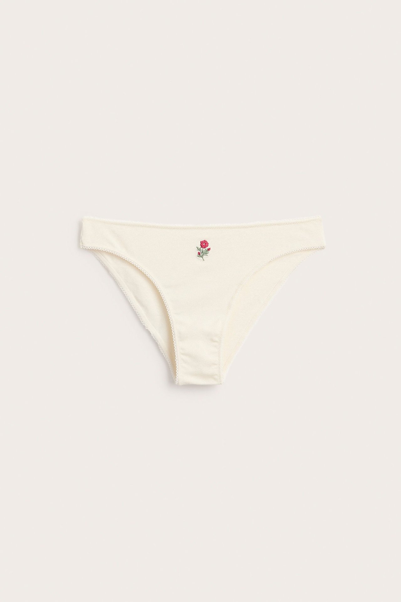 Forfra: Offwhite myk bomulls Brazilian truse med liten brodert rød blomst og bølget kant.