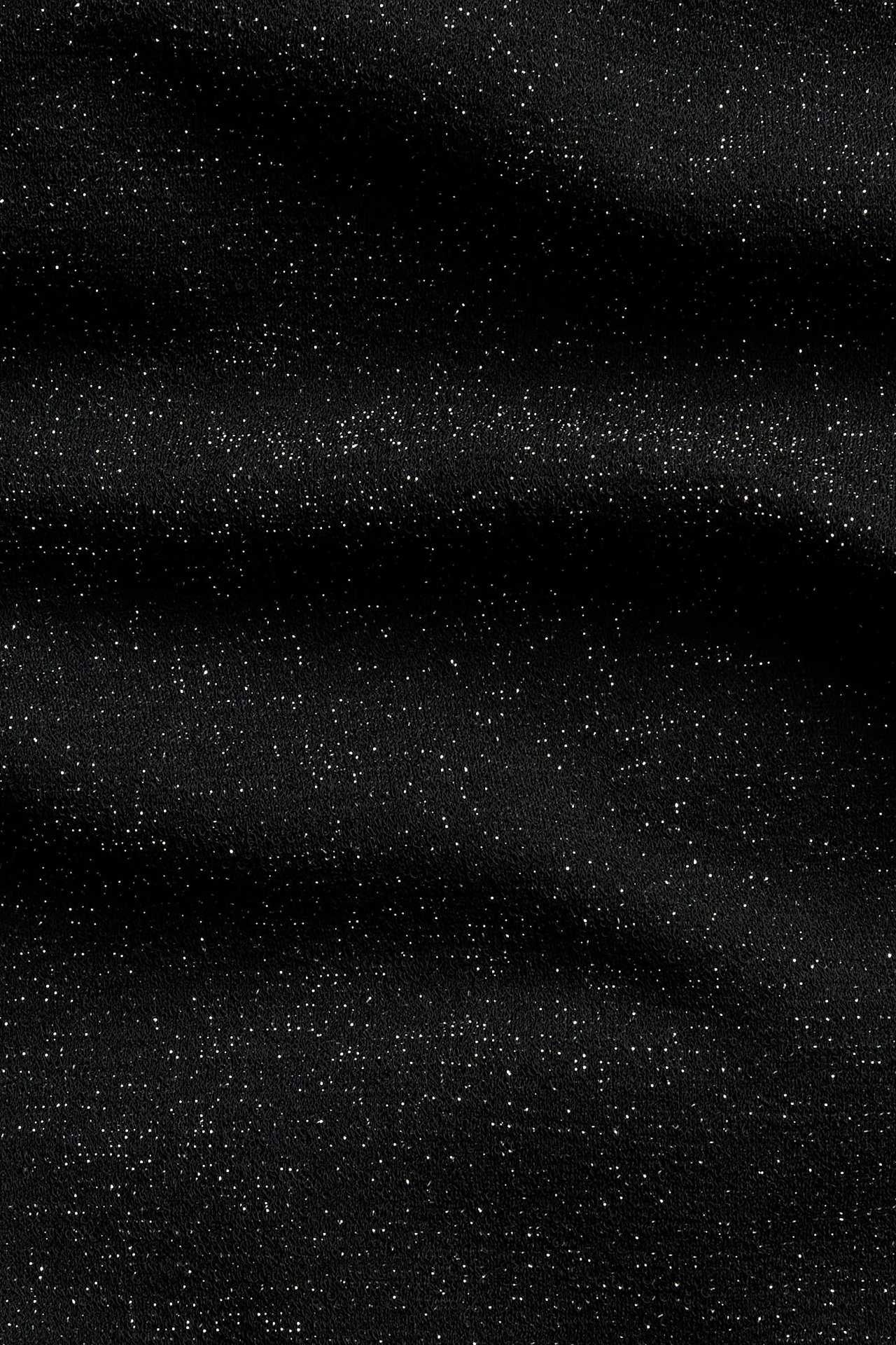 Lähikuva mustasta kankaasta hajanaisella valkoisella glitterillä.