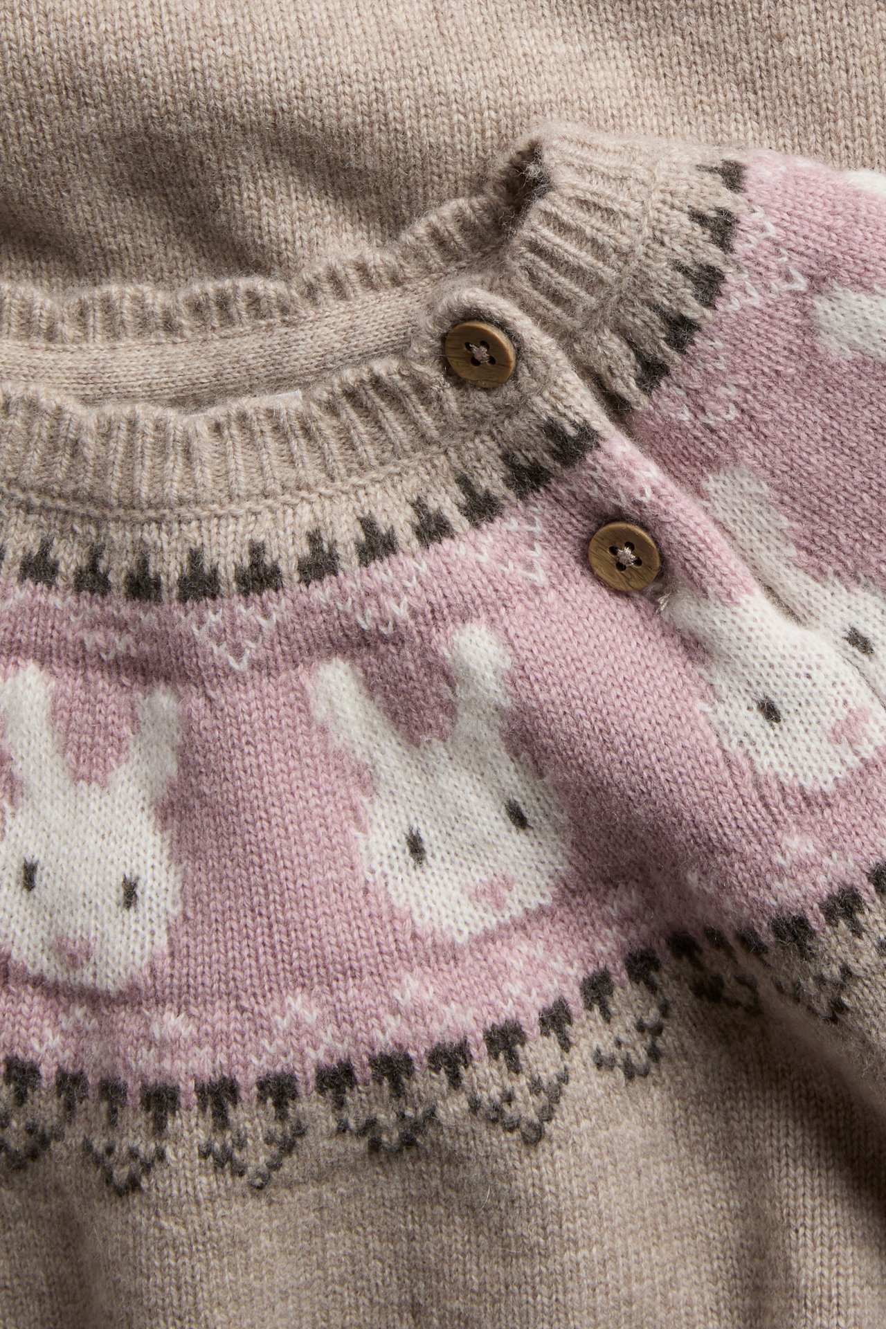 Nærbilde av beige strikket babycardigan med rosa, hvitt og brunt kaninmønster og treknapper.