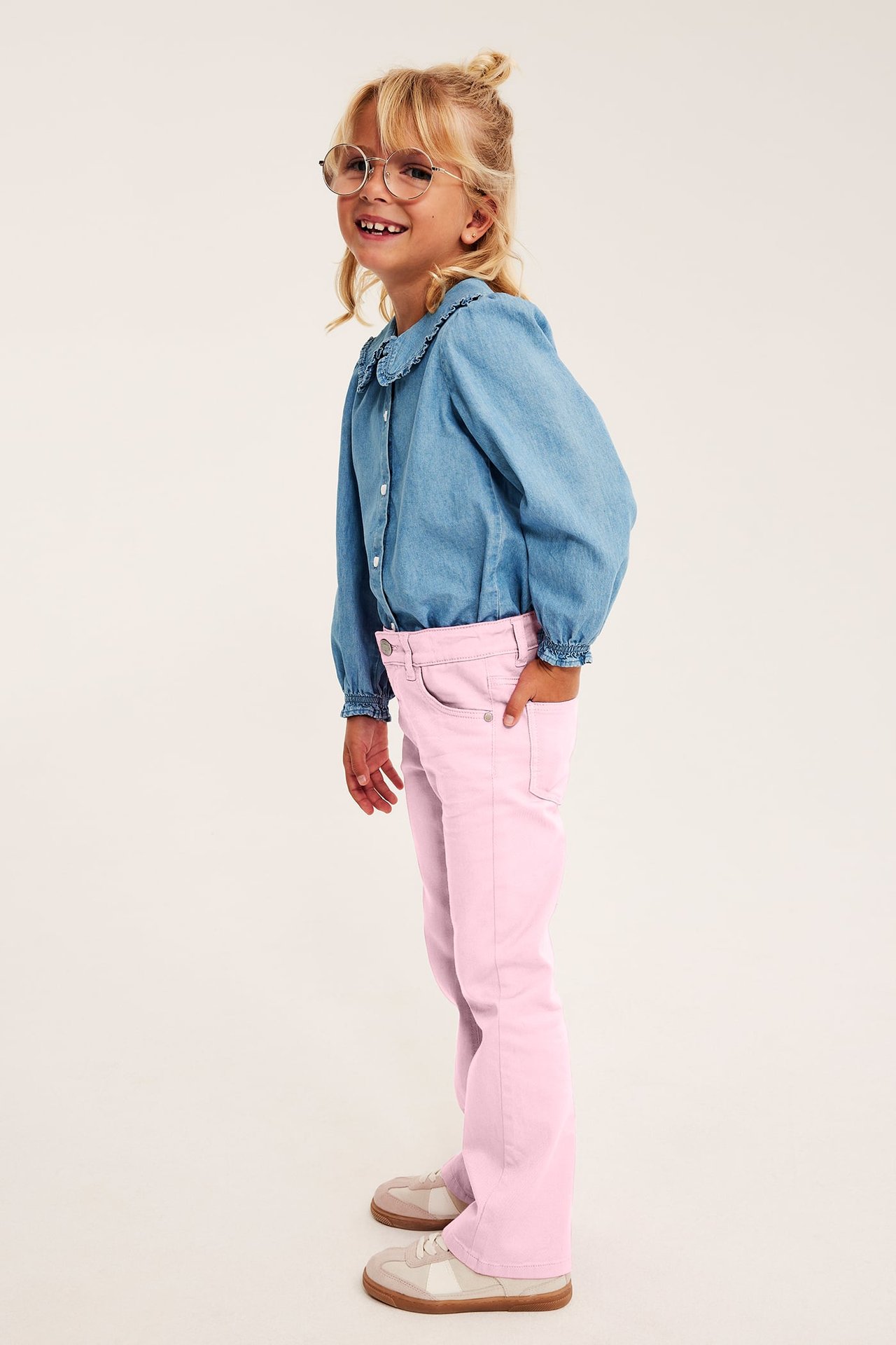Sidovy av ett barn i rosa utsvängda jeans och ljusblå jeansskjorta.