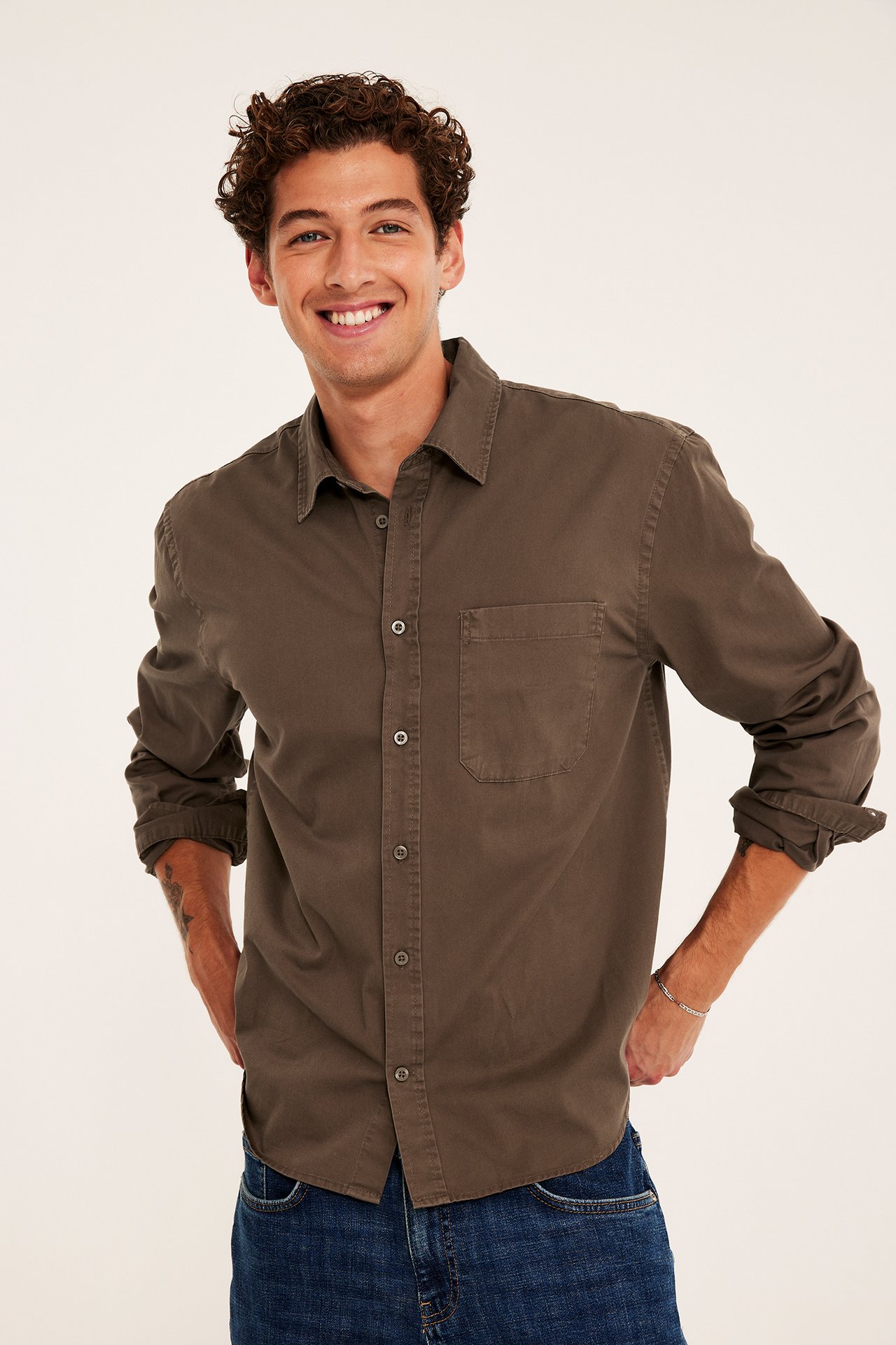 Leende man i khakigrön bomullsskjorta, blå jeans och silverarmband.
