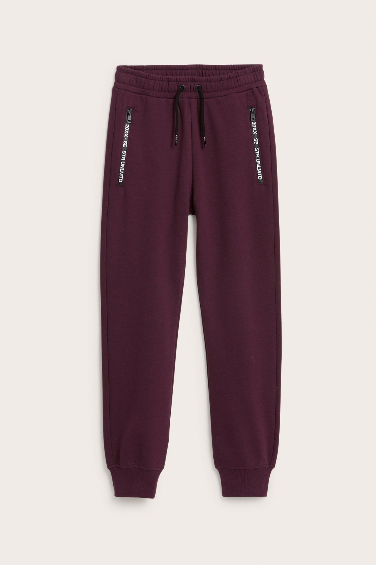Framifrån: vinröda sweatpants med dragsko, ribbade muddar och vertikala dragkedjefickor.