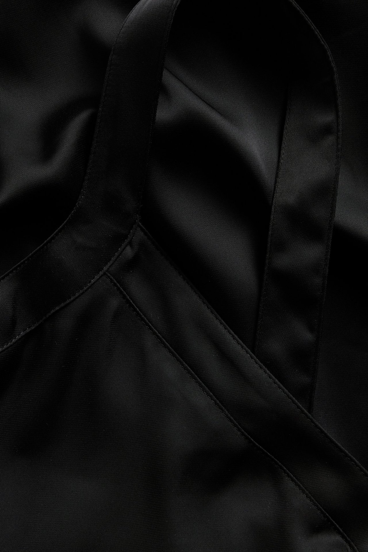 Närbild av ett svart satinlinne i polyester med tunna axelband och V-ringning.