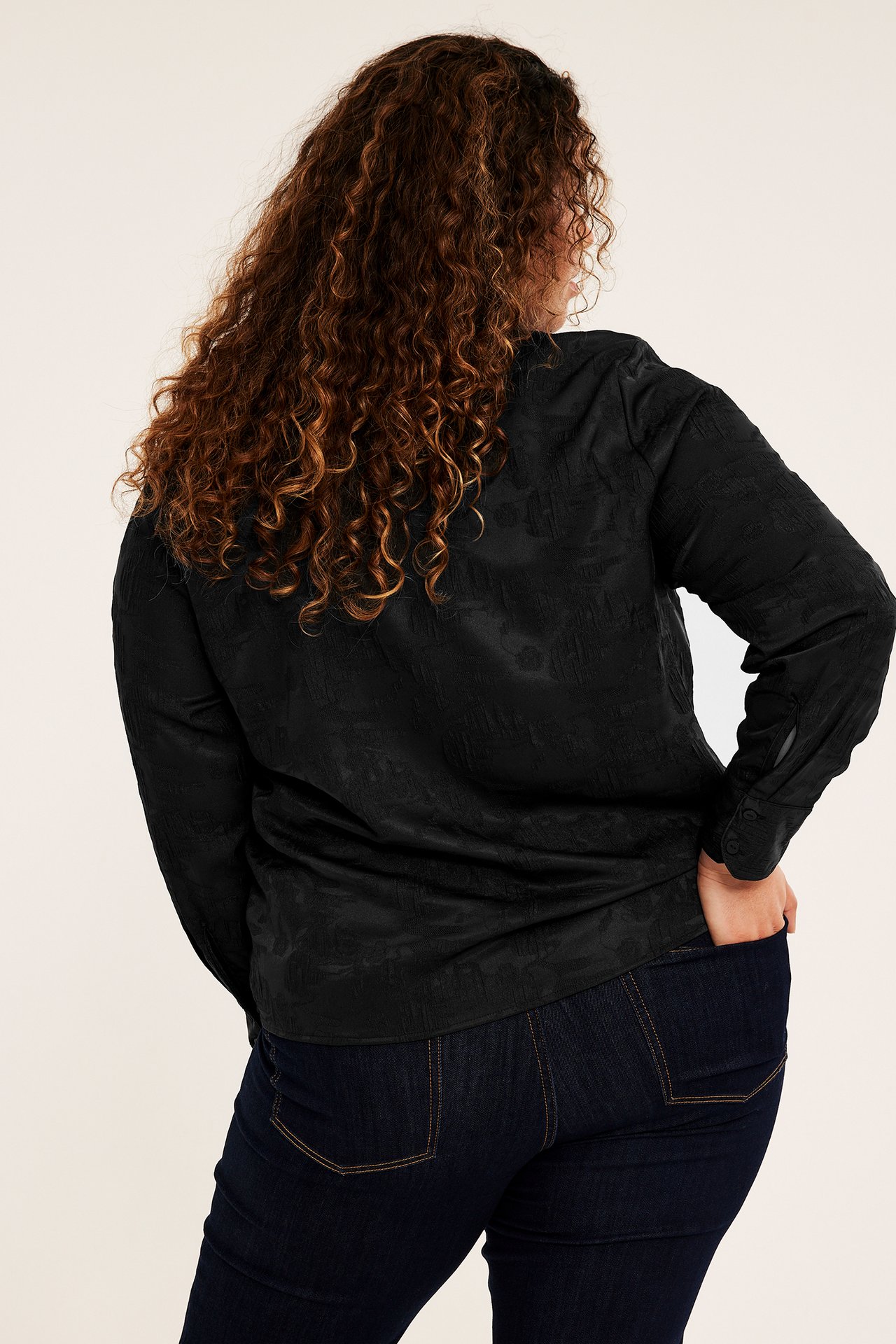 Ryggvy av kvinna i svart mönstrad långärmad skjorta och mörkblå jeans.