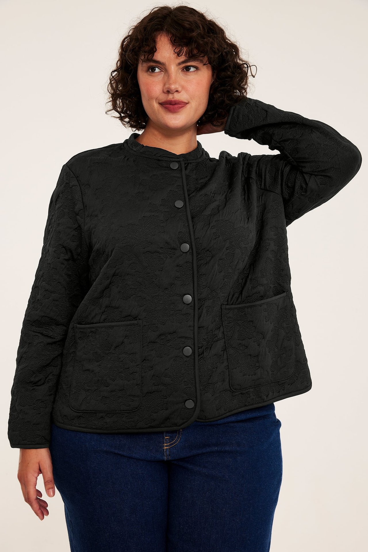 Frontbilde av kvinne i svart teksturert jakke med knapper og blå jeans.