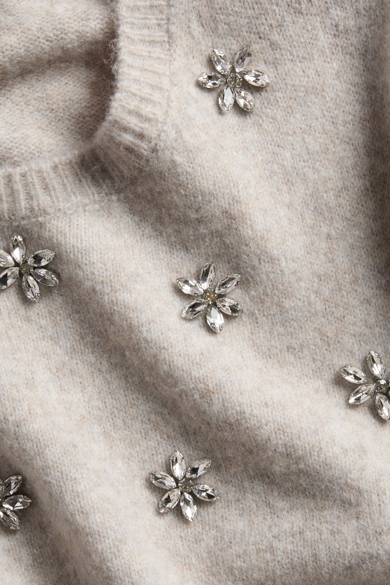 Närbild på en ljusbeige stickad tröja med blommiga kristallutsmyckningar.