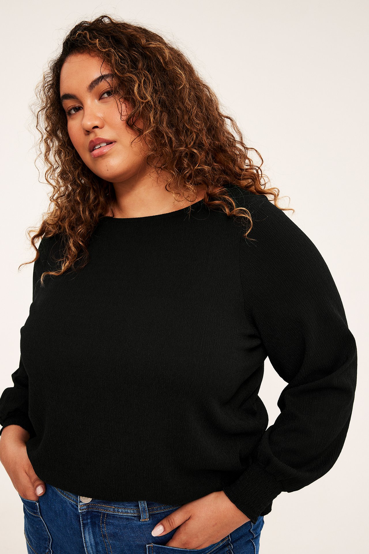 Framifrån, plus-size kvinna i svart texturerad långärmad topp och blå jeans.