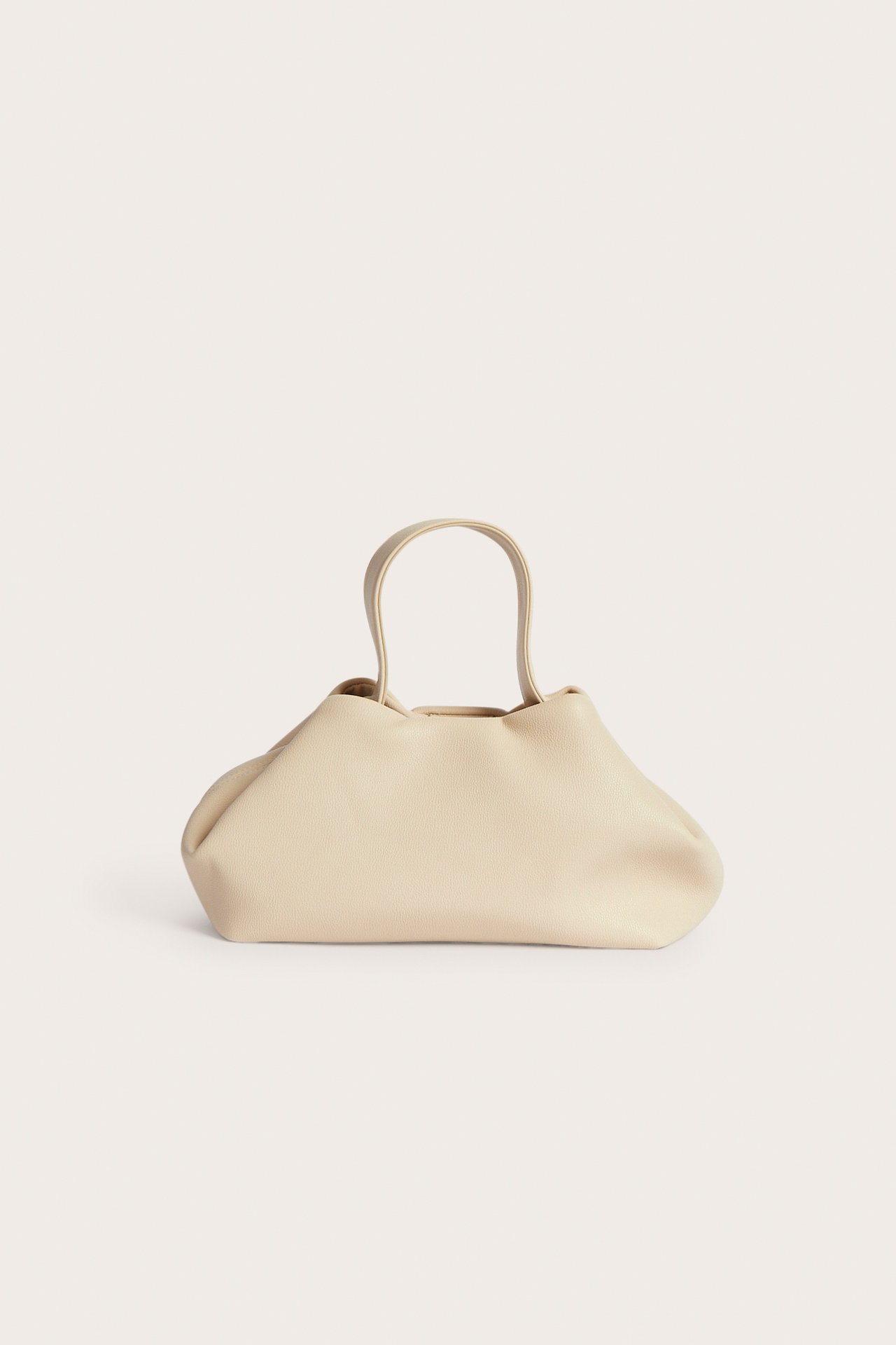 Framifrån en beige mjuk handväska med korta handtag.