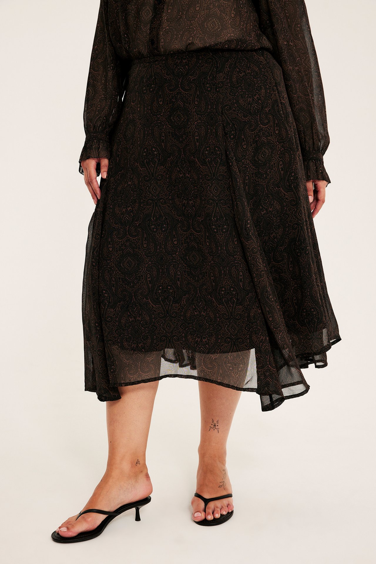 Framifrån: kvinnlig modell i mörk paisley långärmad midiklänning och svarta sandaletter.