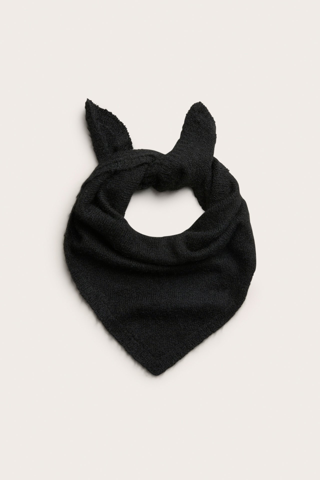 Edestä kuvattu musta neulottu kolmionmallinen bandana, solmittu ylhäältä korvamaisiksi kärjiksi.