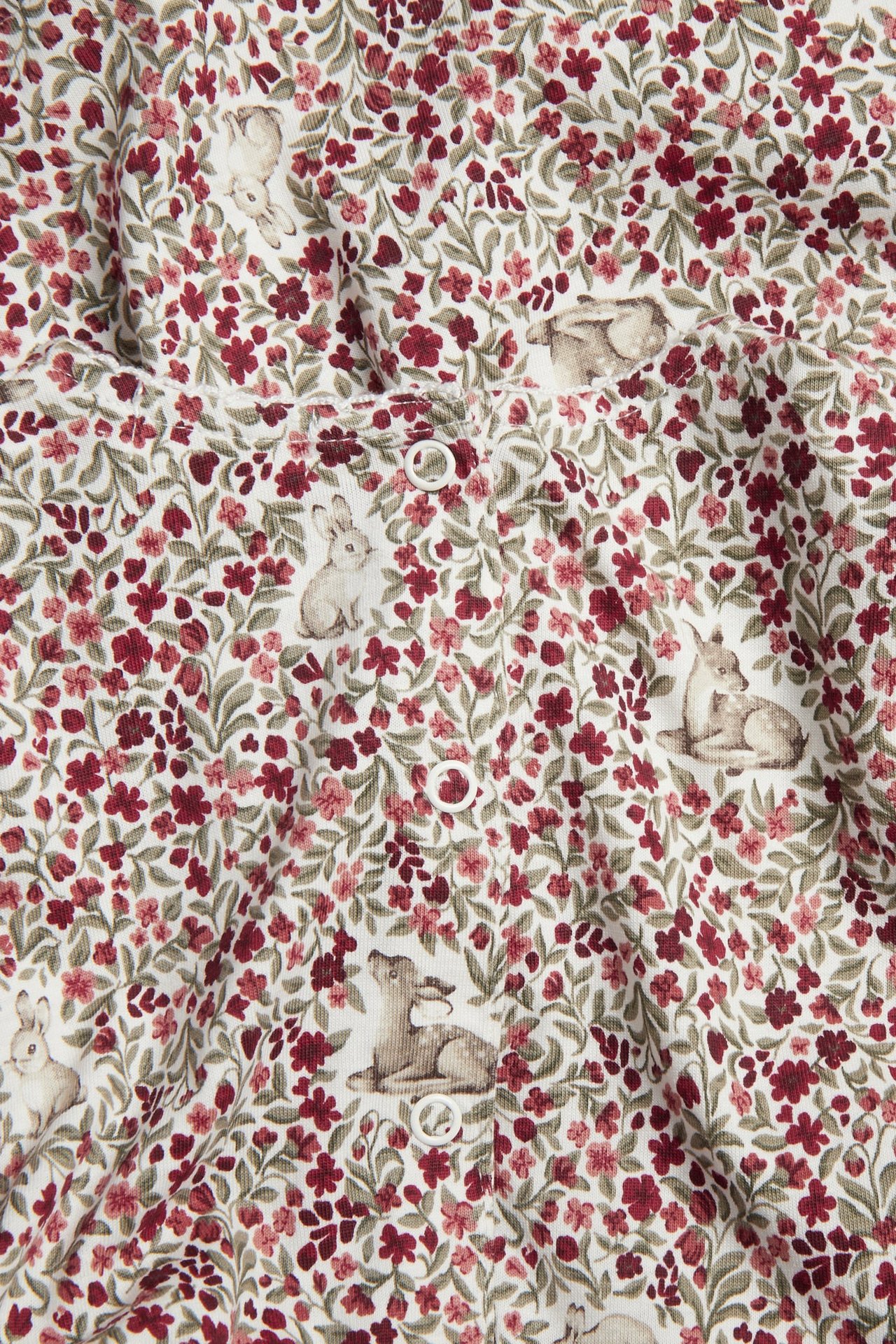 Närbild av vitt ribbat babyplagg med rött blommigt och djurmönster, med vita tryckknappar.