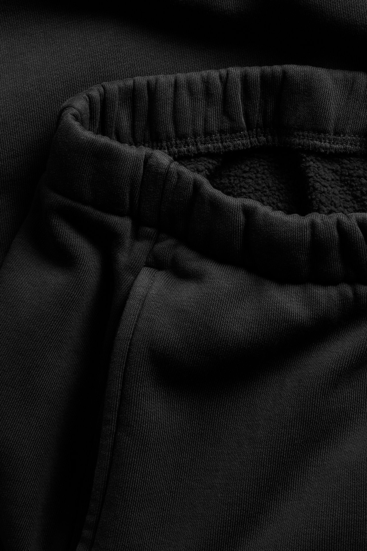 Zbliżenie czarnych dresów z mieszanki bawełny, z elastycznym pasem i detalami kieszeni bocznej.