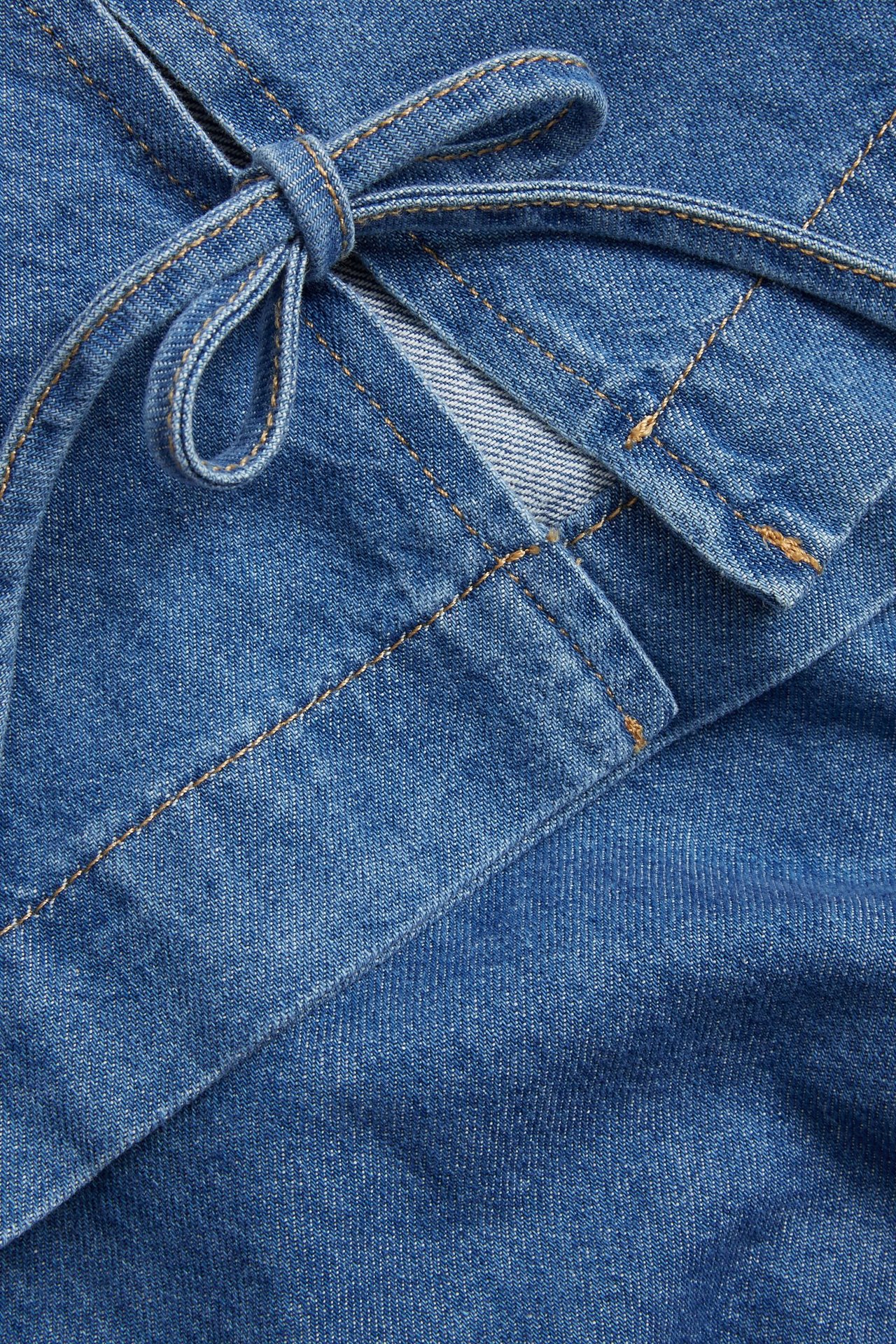 Närbild av ett blått denimplagg, som visar knutna band till en rosett med bruna sömmar.