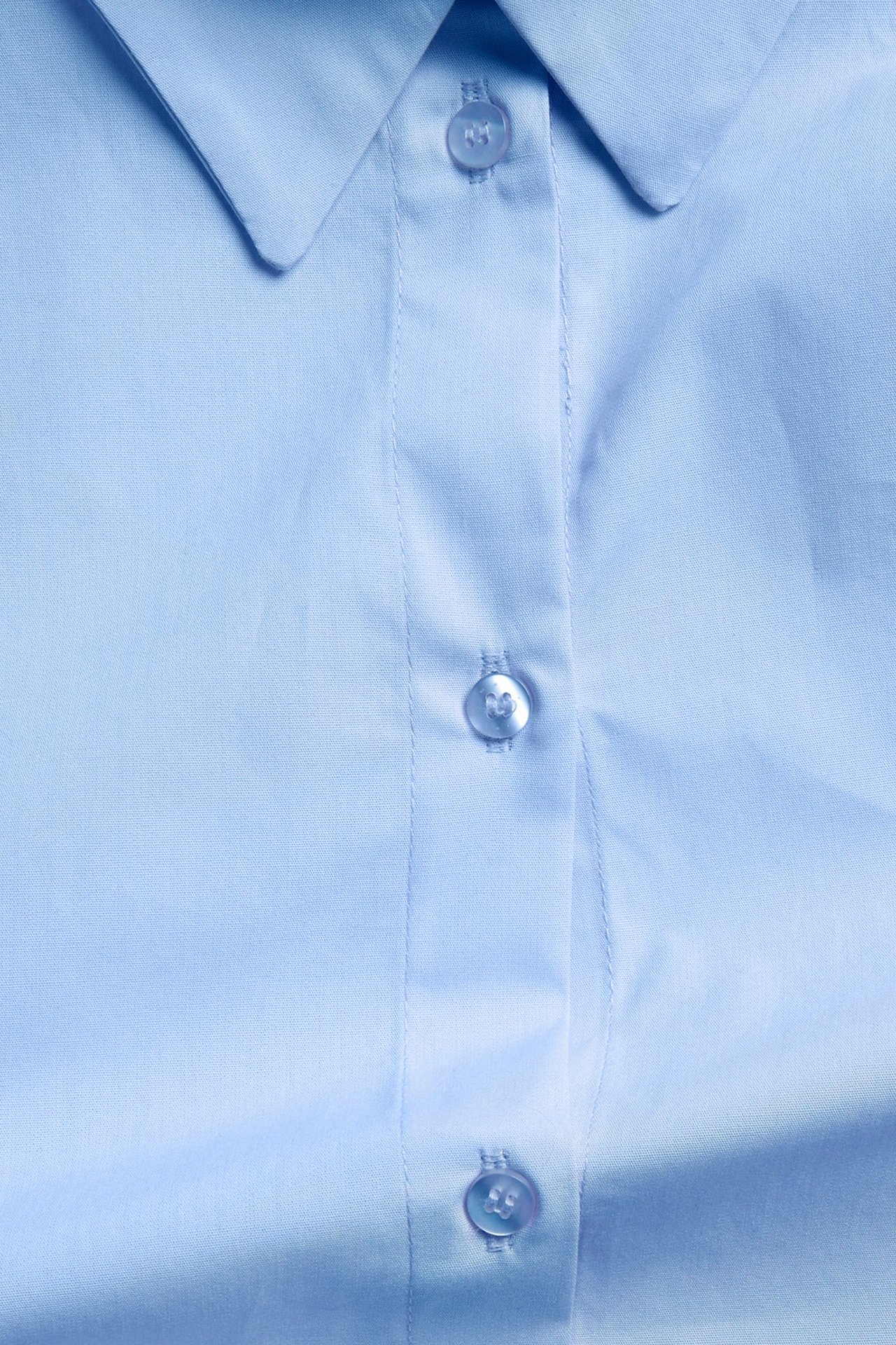 Zbliżenie jasnoniebieskiej koszuli oversize z popeliny bawełnianej, ukazujące kołnierz i guziki.