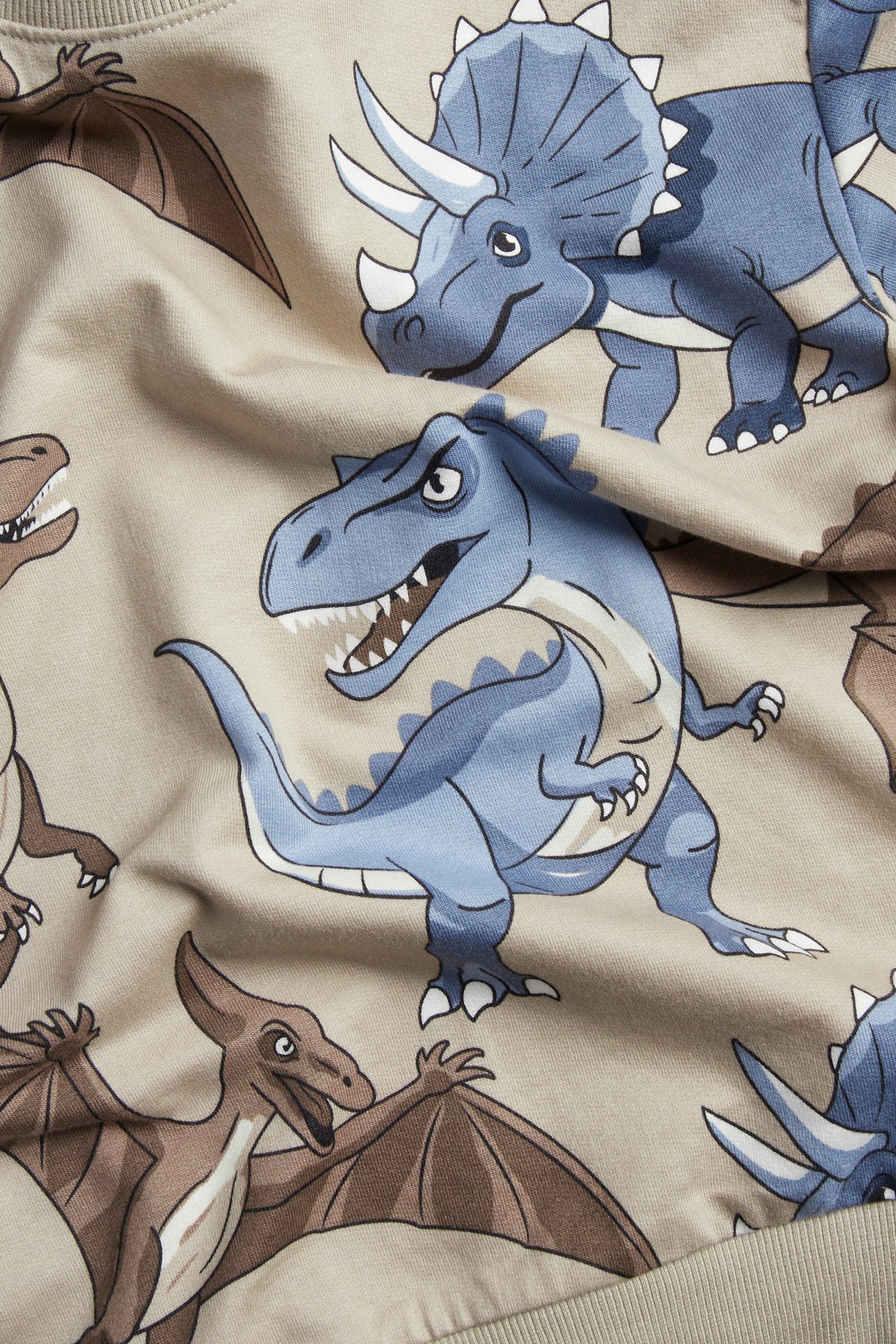 Zbliżenie beżowej tkaniny z kreskówkowym niebieskim i brązowym wzorem dinozaurów, widać ściągacz.