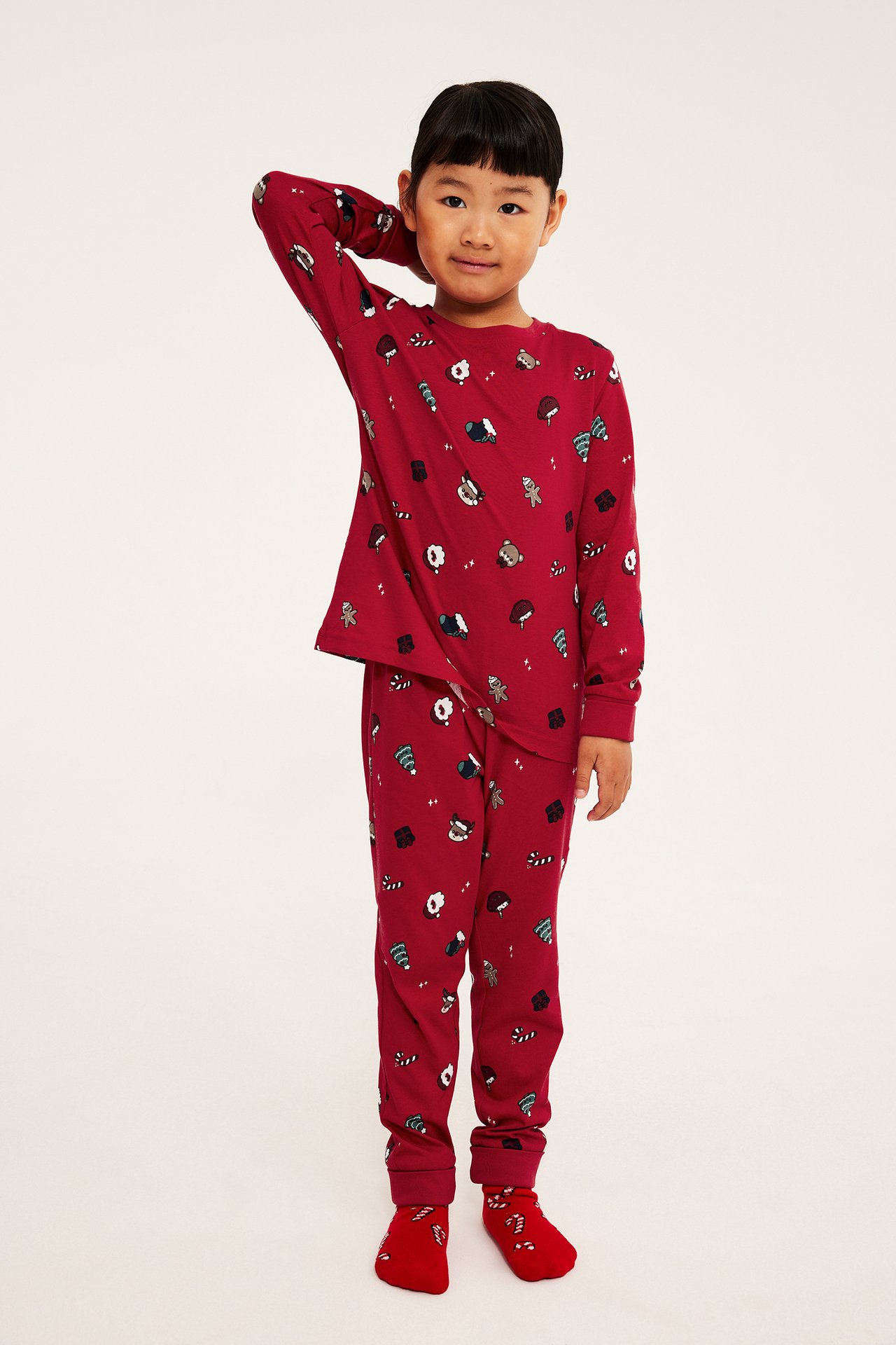 Edestä, lapsi punaisessa jouluaiheisessa pyjamasetissä ja yhteensopivissa sukissa.