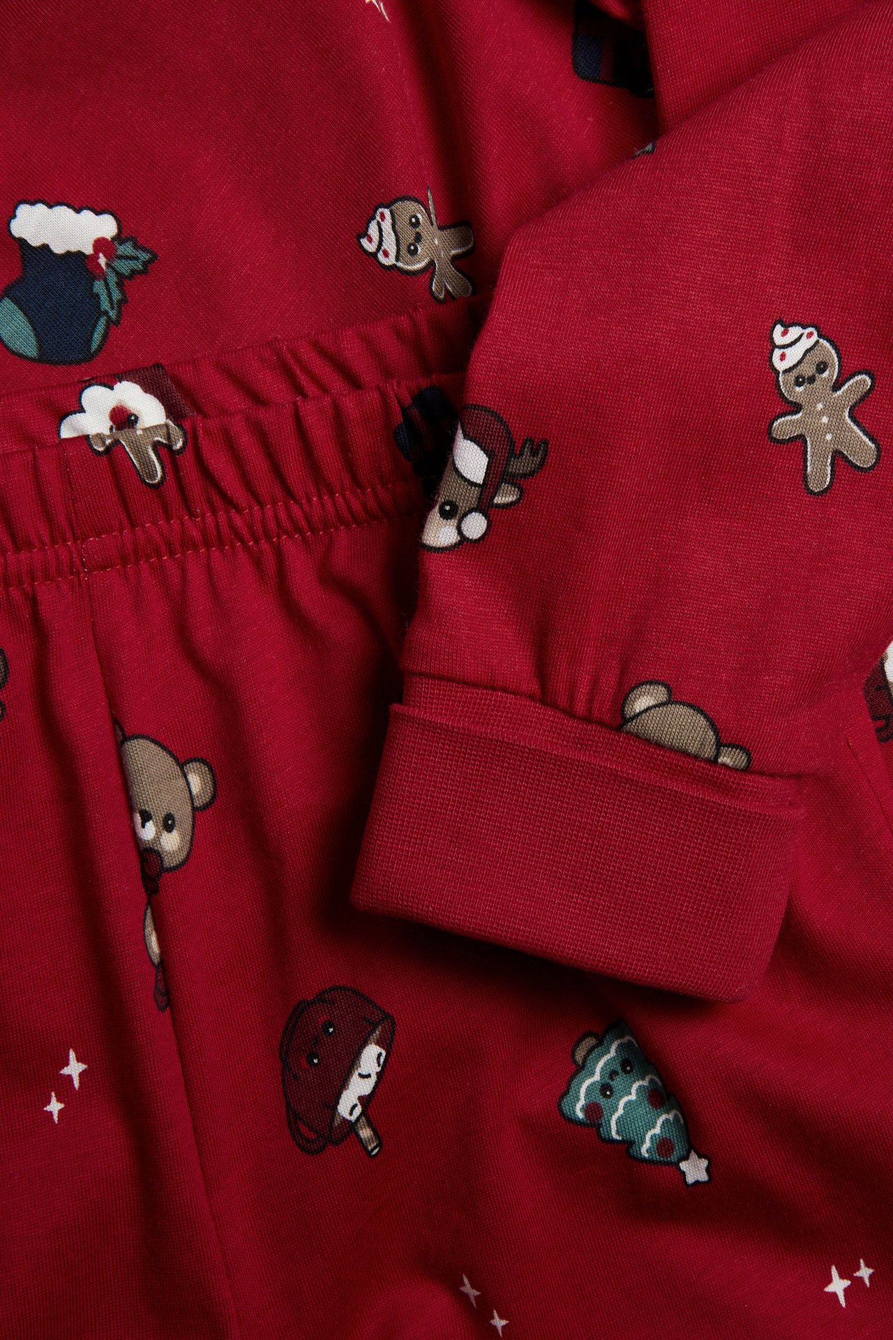 Närbild av röd julmönstrad pyjamas, som visar resår i midjan och manschett på ärmen.