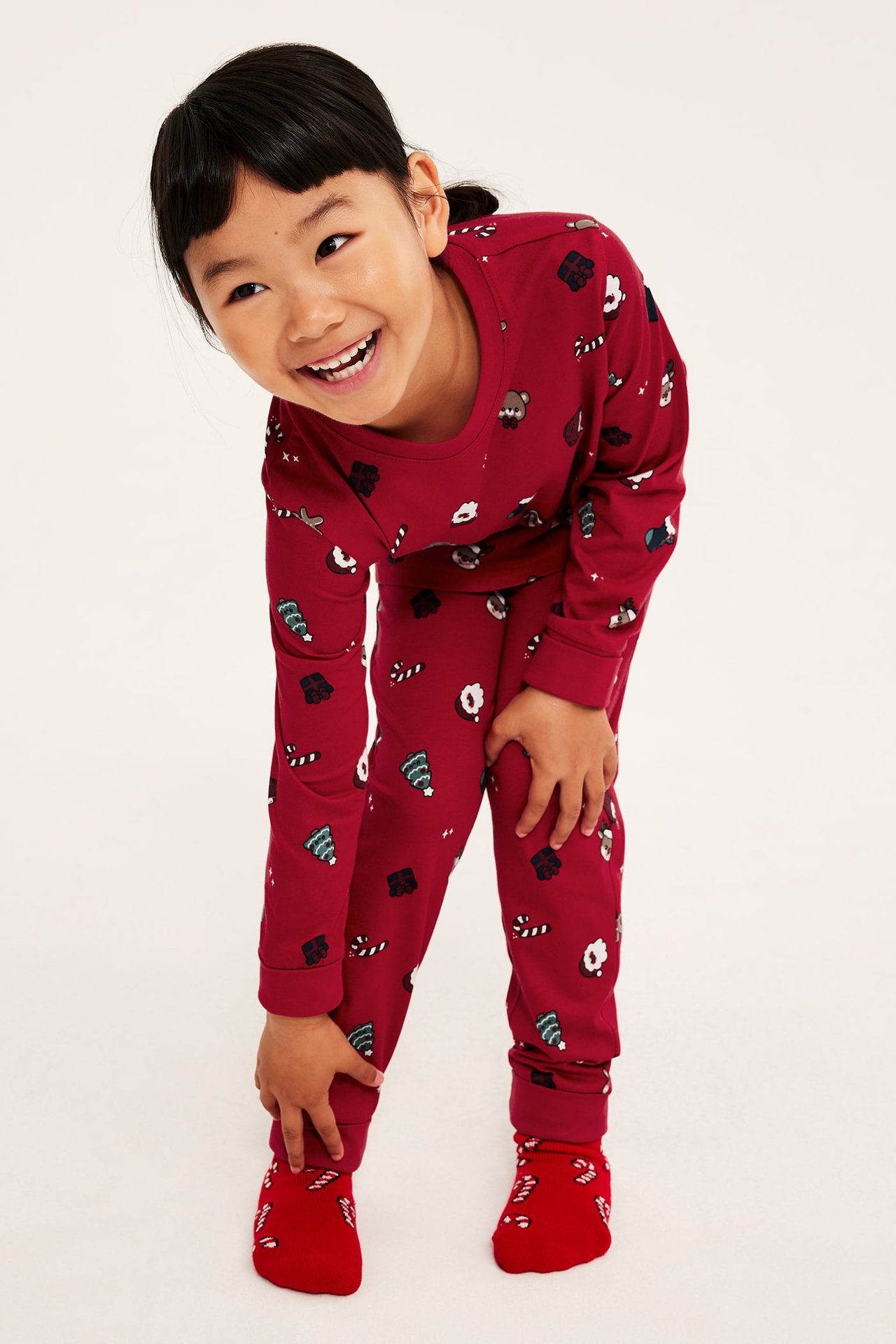 Frontvy av barn i röd mönstrad långärmad pyjamas med polkagrisar och träd, plus röda strumpor.