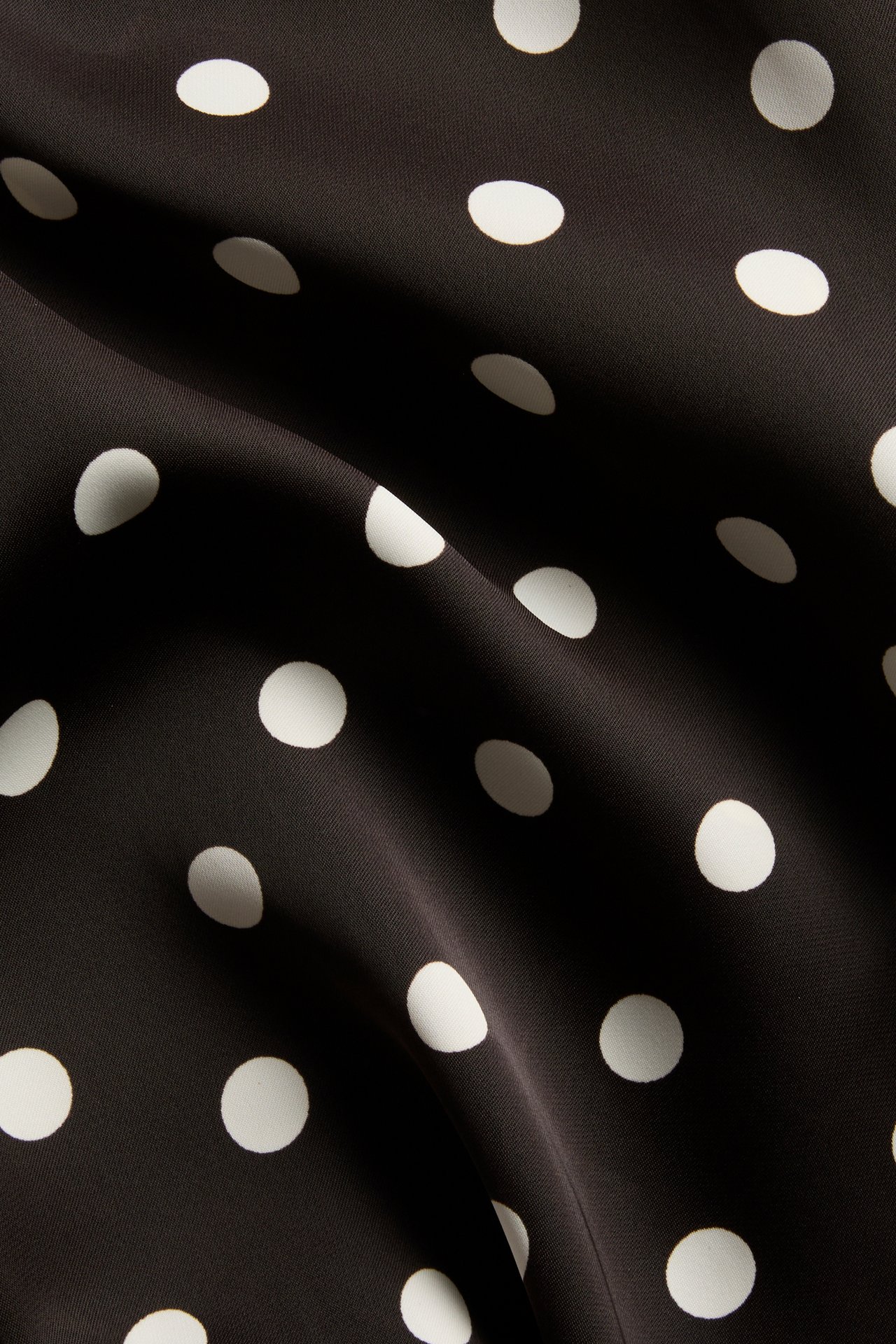 Nærbilde av mørkebrunt satengstoff med hvite prikker.