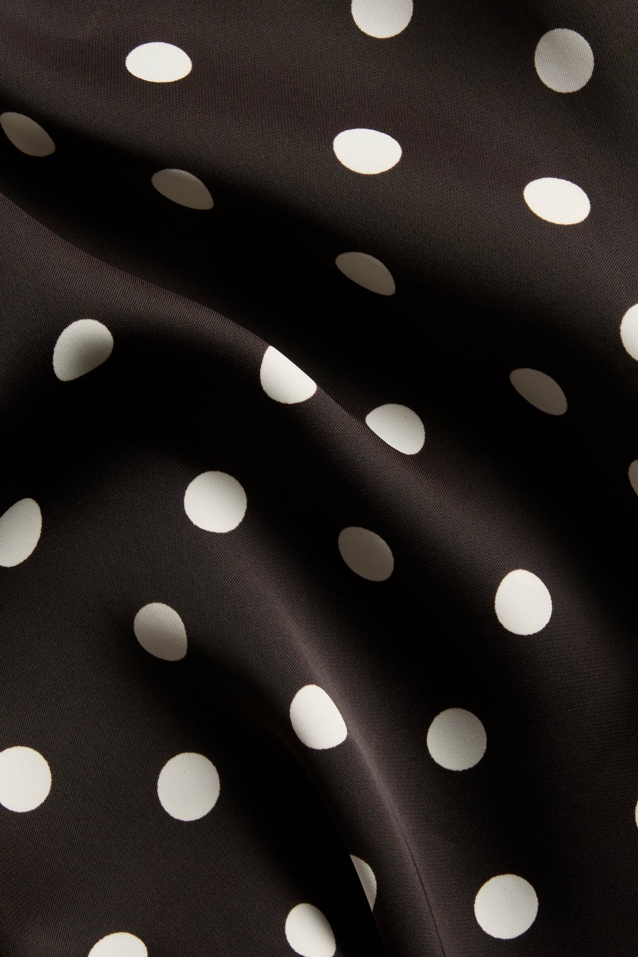 Närbild av mörkbrunt satintyg med vita prickar.